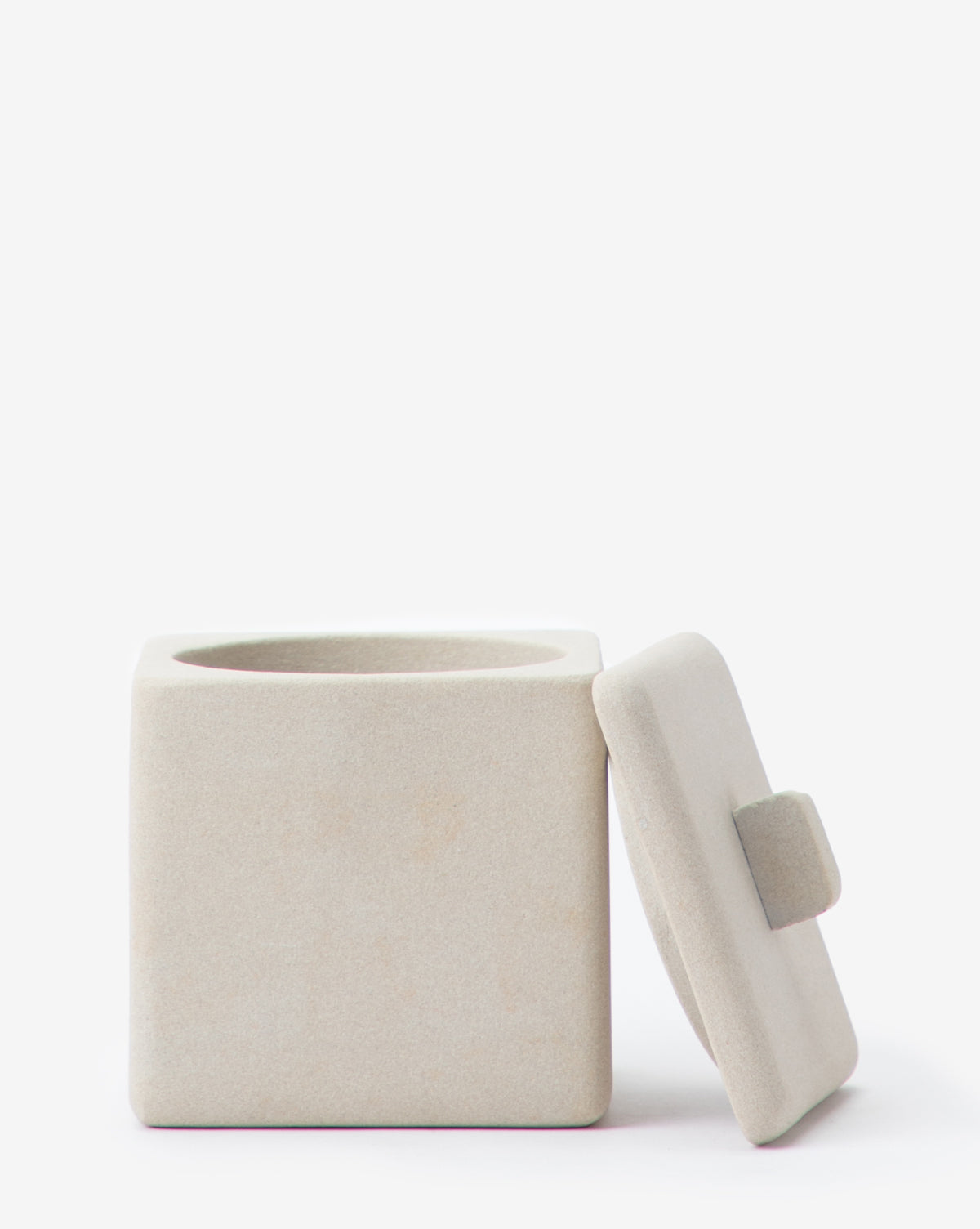 A square, light beige ceramic container with a matching lid and rectangular handle from the Amada Sandstone Bath Collection adds an organic touch to your bathroom decor.