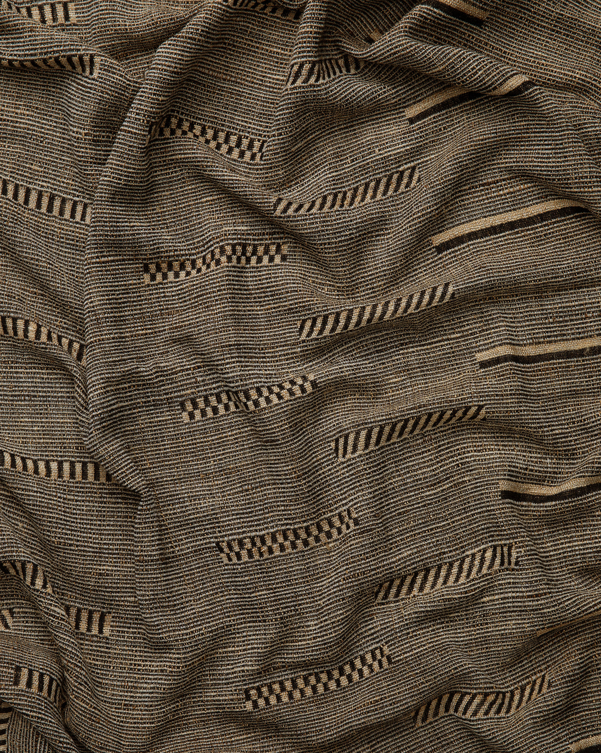 The Anwar Woven Throw features textured brown wool and silk with small black stripes and checkerboard patterns. Its abstract geometric design adds visual interest and cozy elegance, draping beautifully in soft folds.