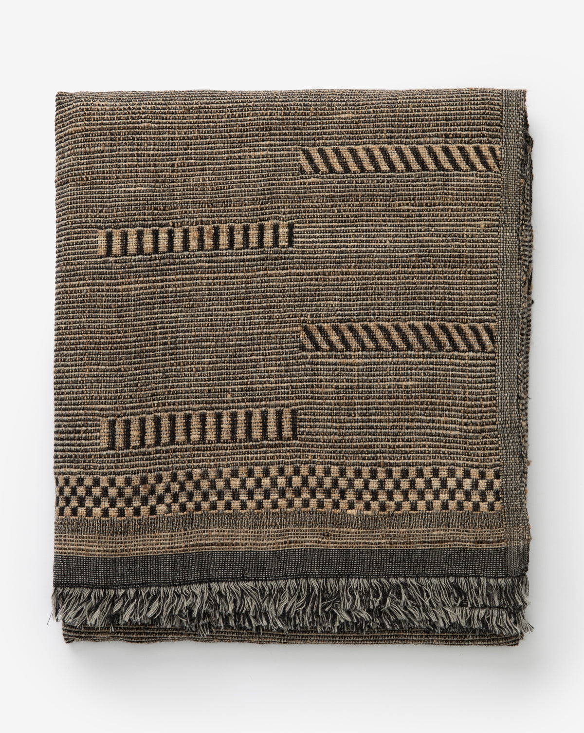 The Anwar Woven Throw is a folded, textured brown and black blanket with geometric patterns—stripes and checkerboards—and elegant fringe along the bottom edge.
