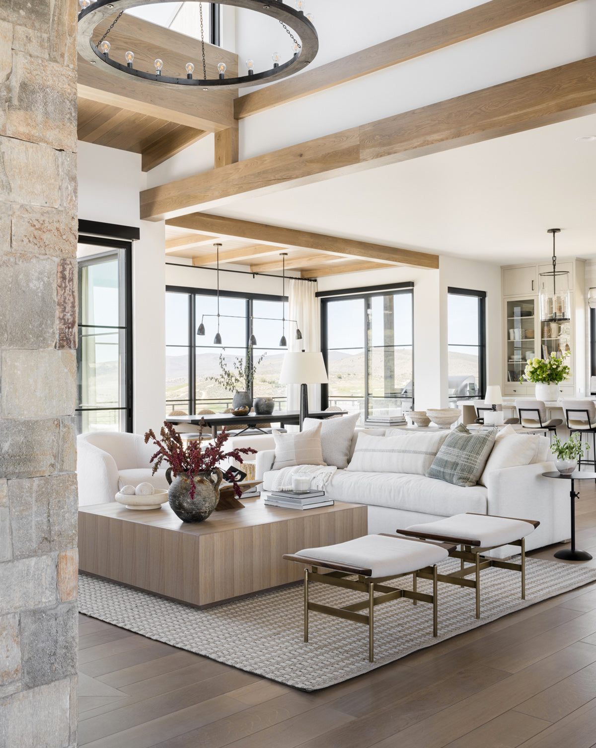 A modern living room features the Macy Upholstered Sofa (84-96), a large wooden coffee table, neutral decor, and floor-to-ceiling windows. Exposed beams and soft natural light create a cozy, elegant atmosphere by McGee & Co.
