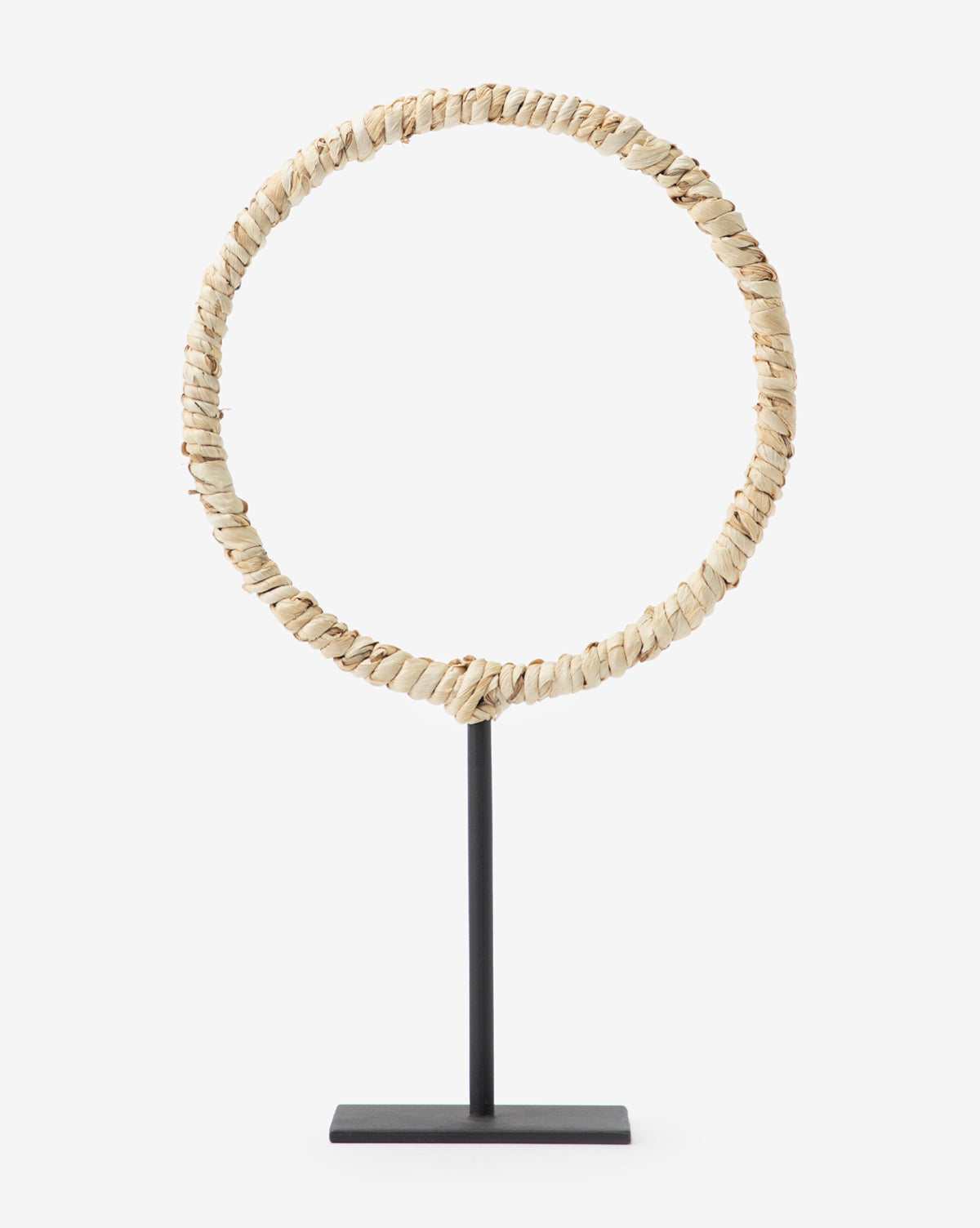 The Brayden Woven Object features a corn husk texture in a circular design, mounted upright on a black metal stand with a rectangular base, adding contemporary style to any space.