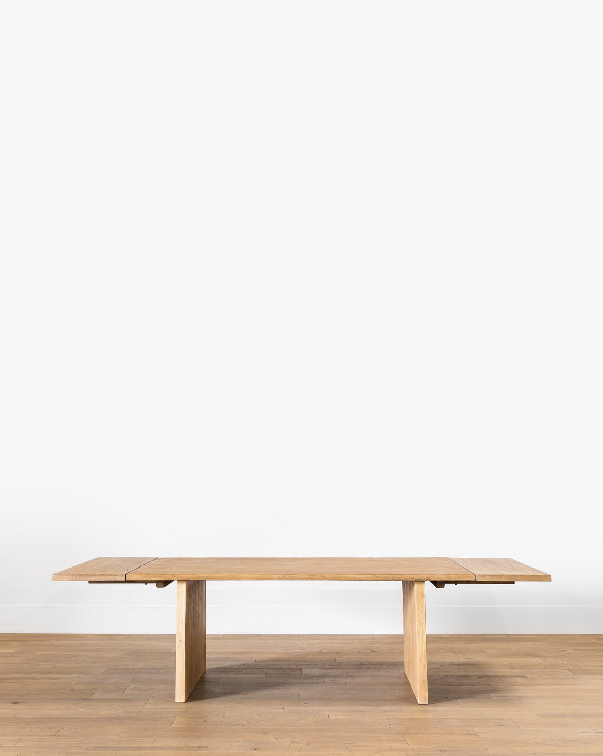 The Dillon Extension Dining Table, a long rectangular piece with simple, clean lines crafted from reclaimed elm, sits on a light wood floor against a plain white wall by McGee & Co.