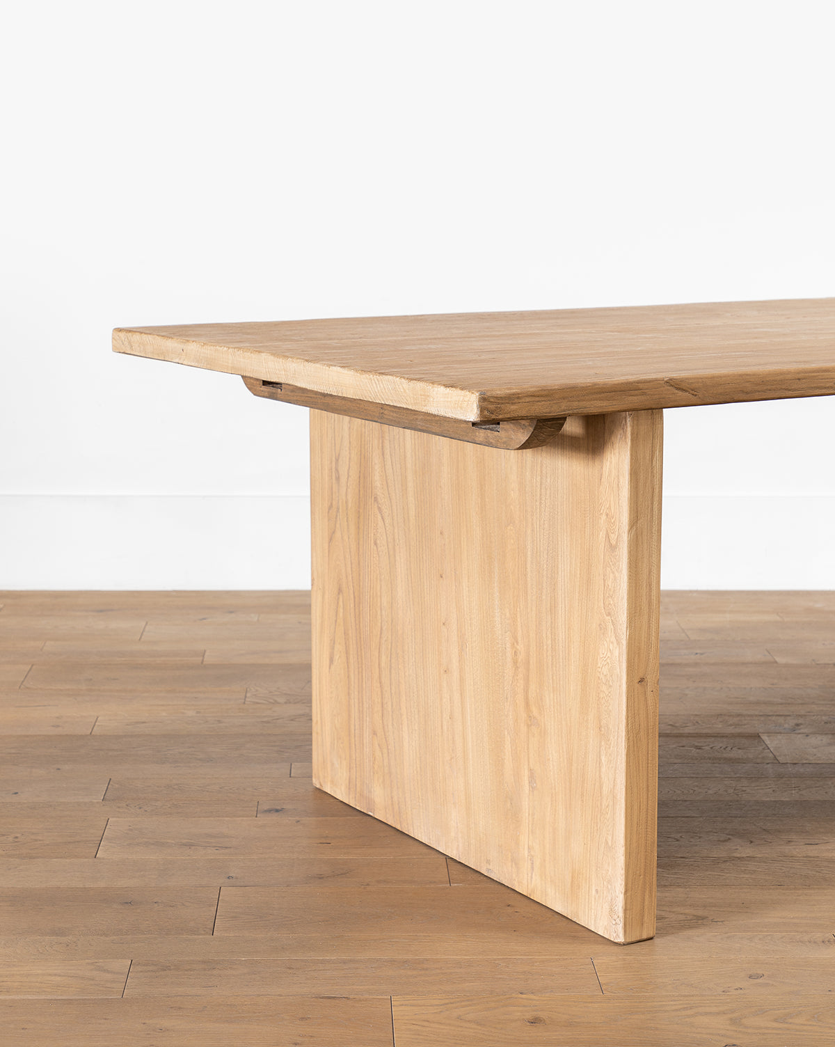 The Dillon Extension Dining Table features a thick rectangular top and wide, flat legs, creating a modern rustic look, shown on a wooden floor against a plain white wall by McGee & Co.