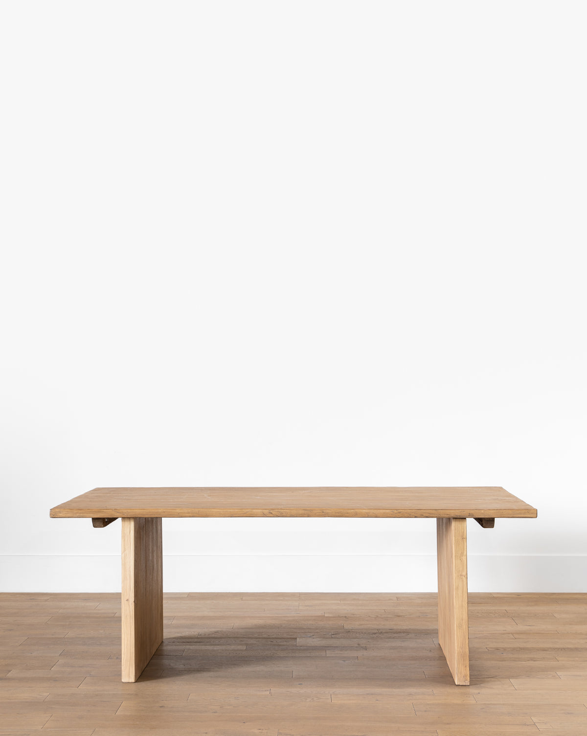 The Dillon Extension Dining Table features a minimalist reclaimed elm design with a rectangular top and two wide, flat legs, set on a light wood floor against a plain white wall, by McGee & Co.