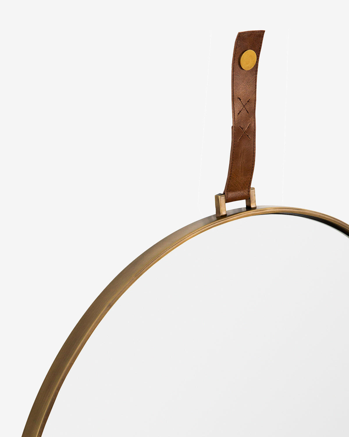 The Laila Circle Mirror features a brass frame and circular design, suspended by a brown stitched leather hanger with a brass fastener, standing out elegantly against a white background, by McGee & Co.