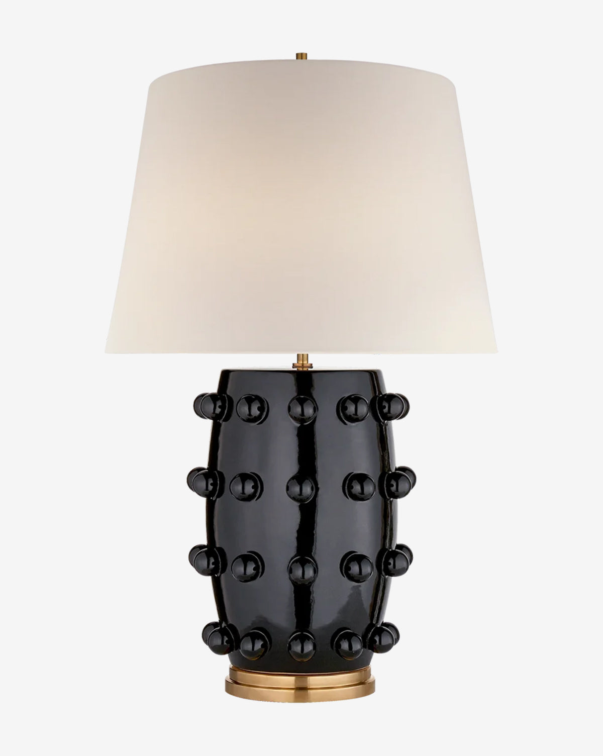 The Linden Table Lamp has a white linen shade, a glossy black porcelain base with raised round knobs, and sits on a gold-colored circular stand, by McGee & Co.