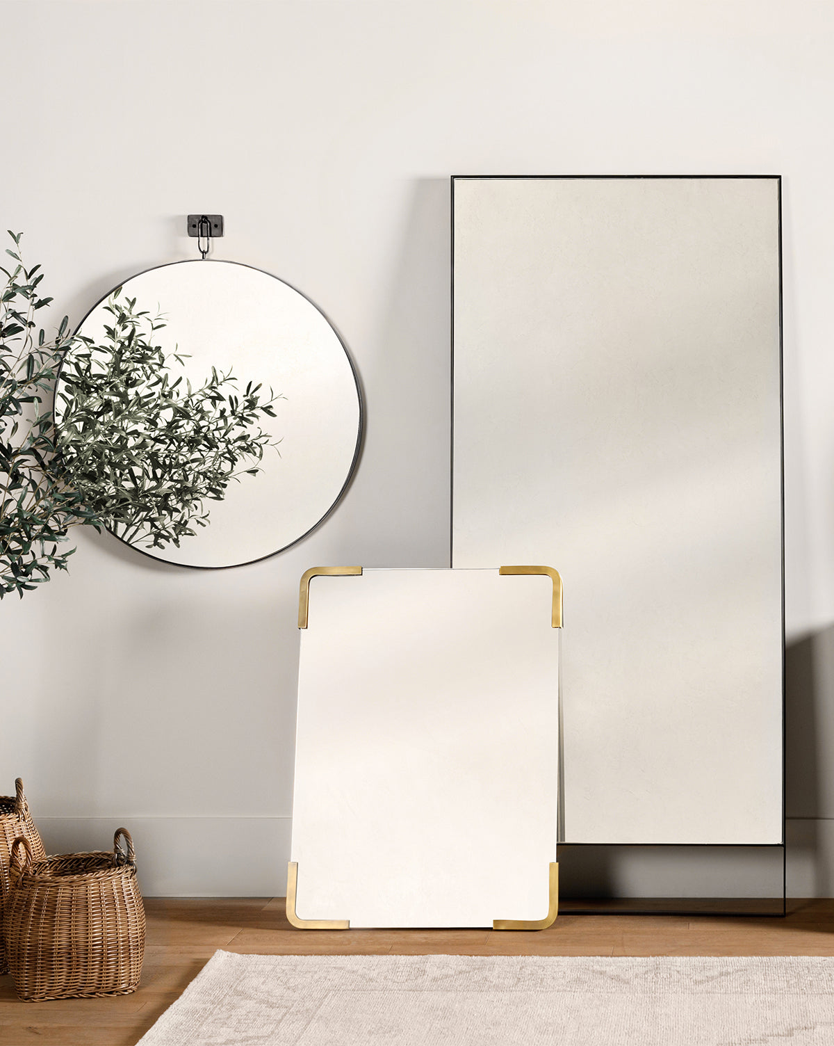 A minimalist room features the Mare Mirror, a round frameless mirror, and a small rectangular mirror with gold corners. A woven basket and a plant bring warmth to the neutral, modern decor, by McGee & Co.