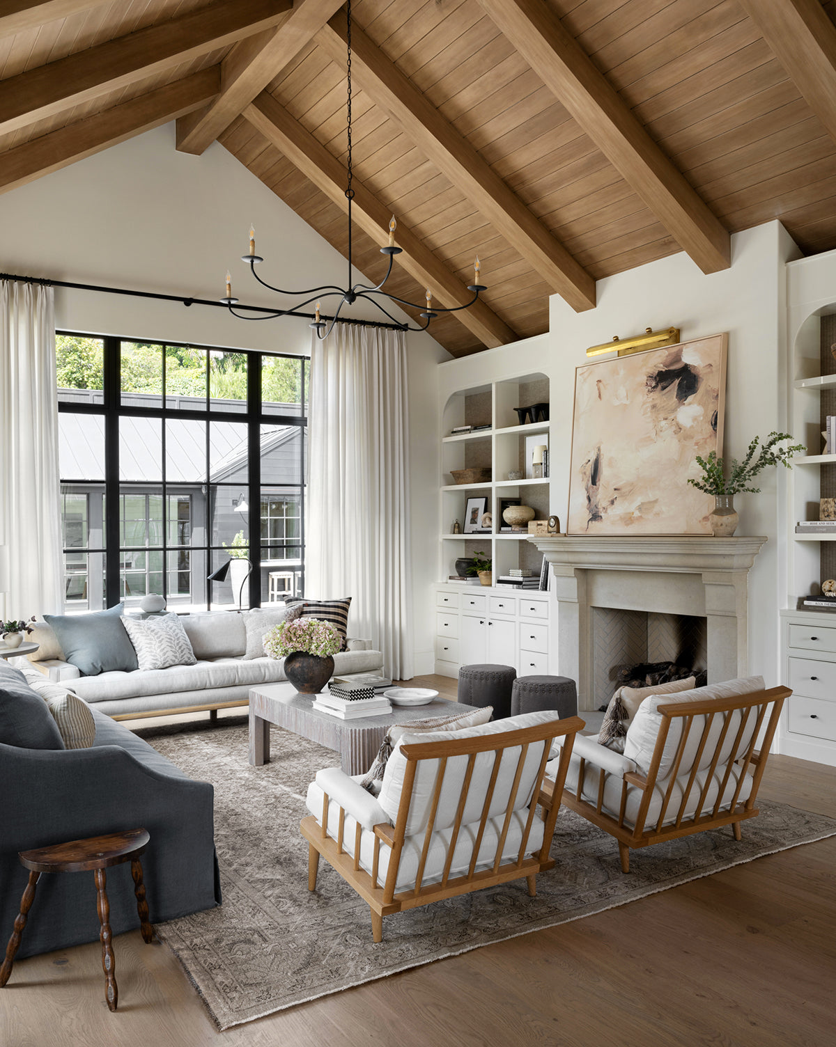 A spacious living room features a vaulted wood ceiling, light walls, and black-framed windows. Cozy seating surrounds a fireplace with built-ins, highlighted by the Warm Abstract artwork that enhances the inviting atmosphere.