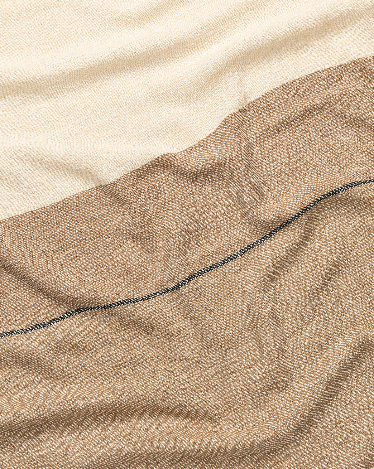 A close-up of the Murphy Silk Throw highlights its cream and light brown sections, divided by a slim dark line. Hand-loomed, the throw features gentle folds and an exceptionally soft texture.