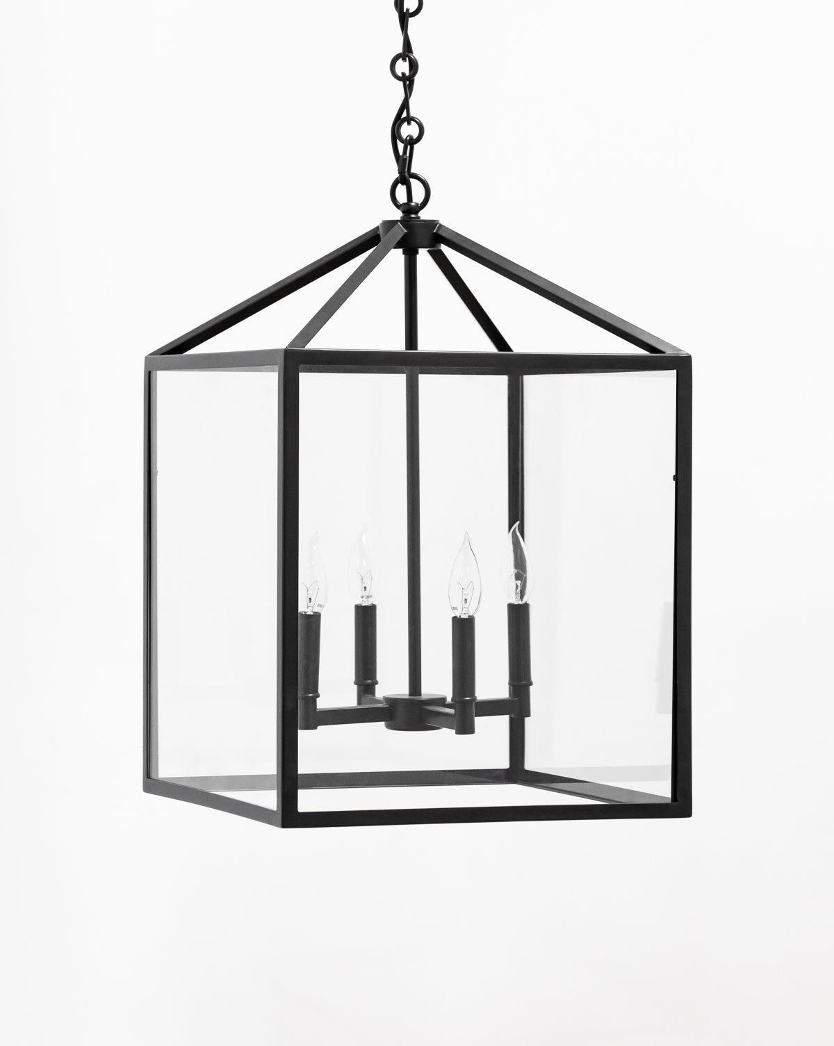 The Makerspalm Pietro Lantern Pendant is a black metal geometric chandelier with clear glass panels, featuring four candle-style bulbs in a rectangular frame, suspended by a chain. McGee & Co.
