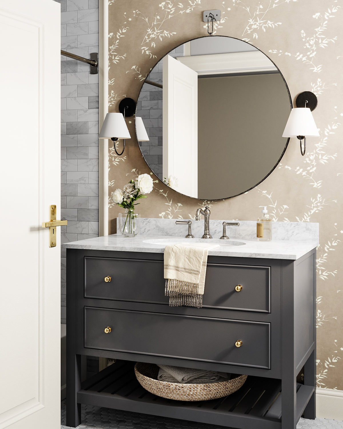 A modern bathroom vanity with a marble countertop, gray drawers with gold knobs, the Haven Wall Mirror, two wall sconces, a towel, and a vase of white flowers. The wallpaper has a subtle floral pattern by McGee & Co.
