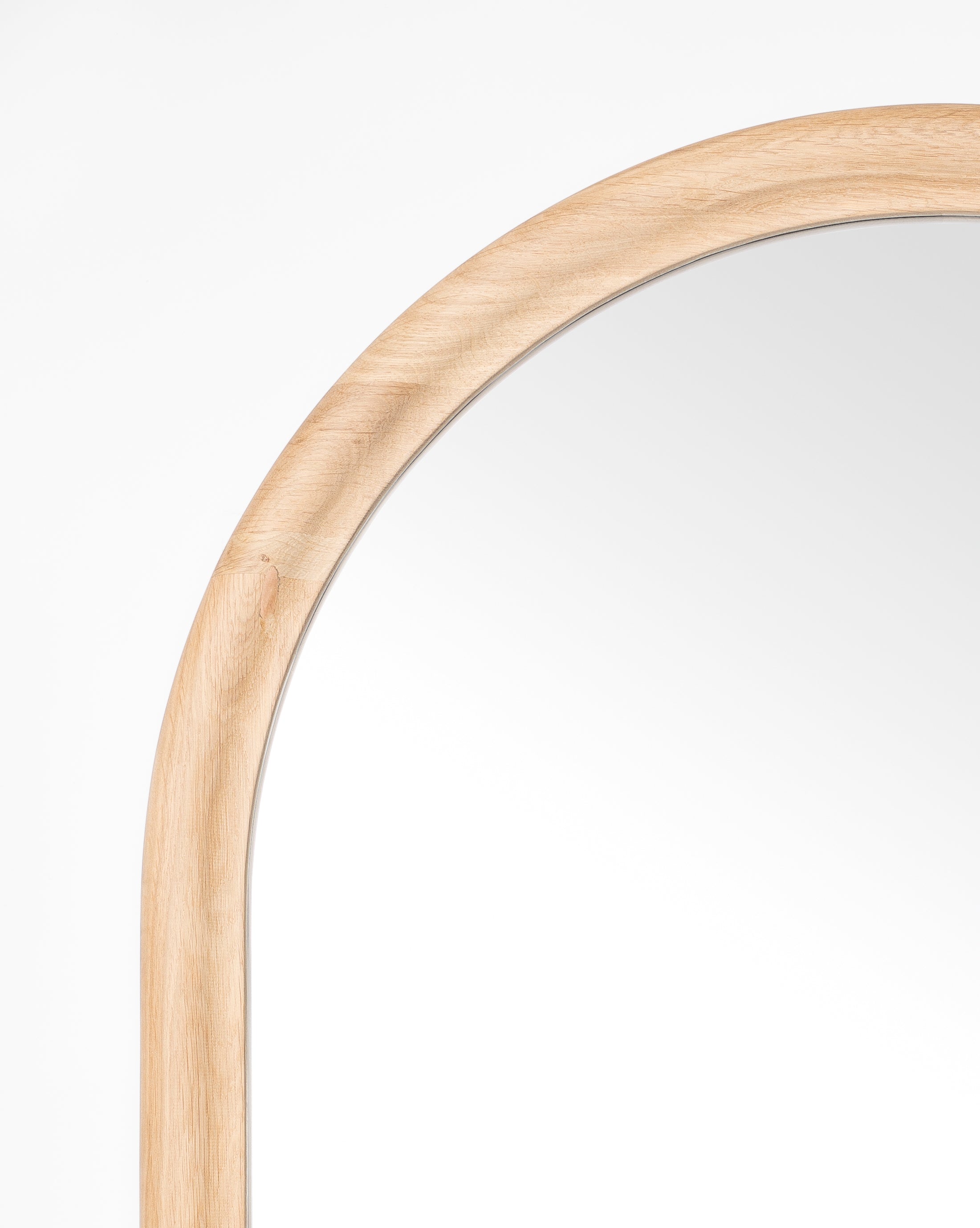 A close-up of the upper left corner of the Reta Arched Wall Mirror, showcasing its light natural oak frame and arched design, set against a plain white background, by McGee & Co.