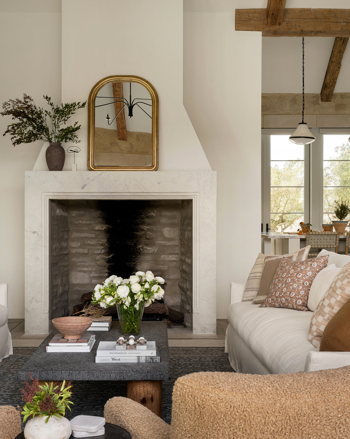 A cozy living room features a stone fireplace with a gold-framed mirror above, and Theoden Terracotta Bowl on the black coffee table. Neutral sofas with patterned pillows complete the rustic, inviting atmosphere.