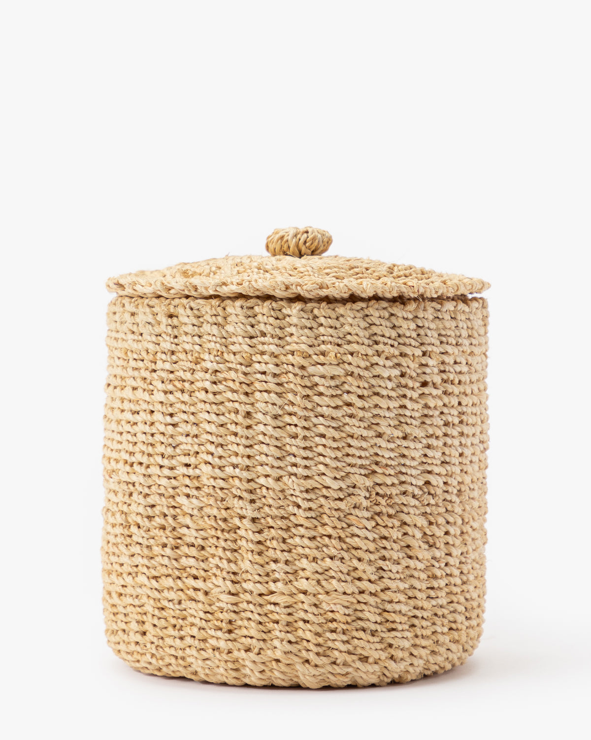 The Thalia Woven Canister is a round abaca piece with a lid and small handle, crafted from natural straw—ideal for organic storage or as bathroom counter decor—shown on a plain white background.