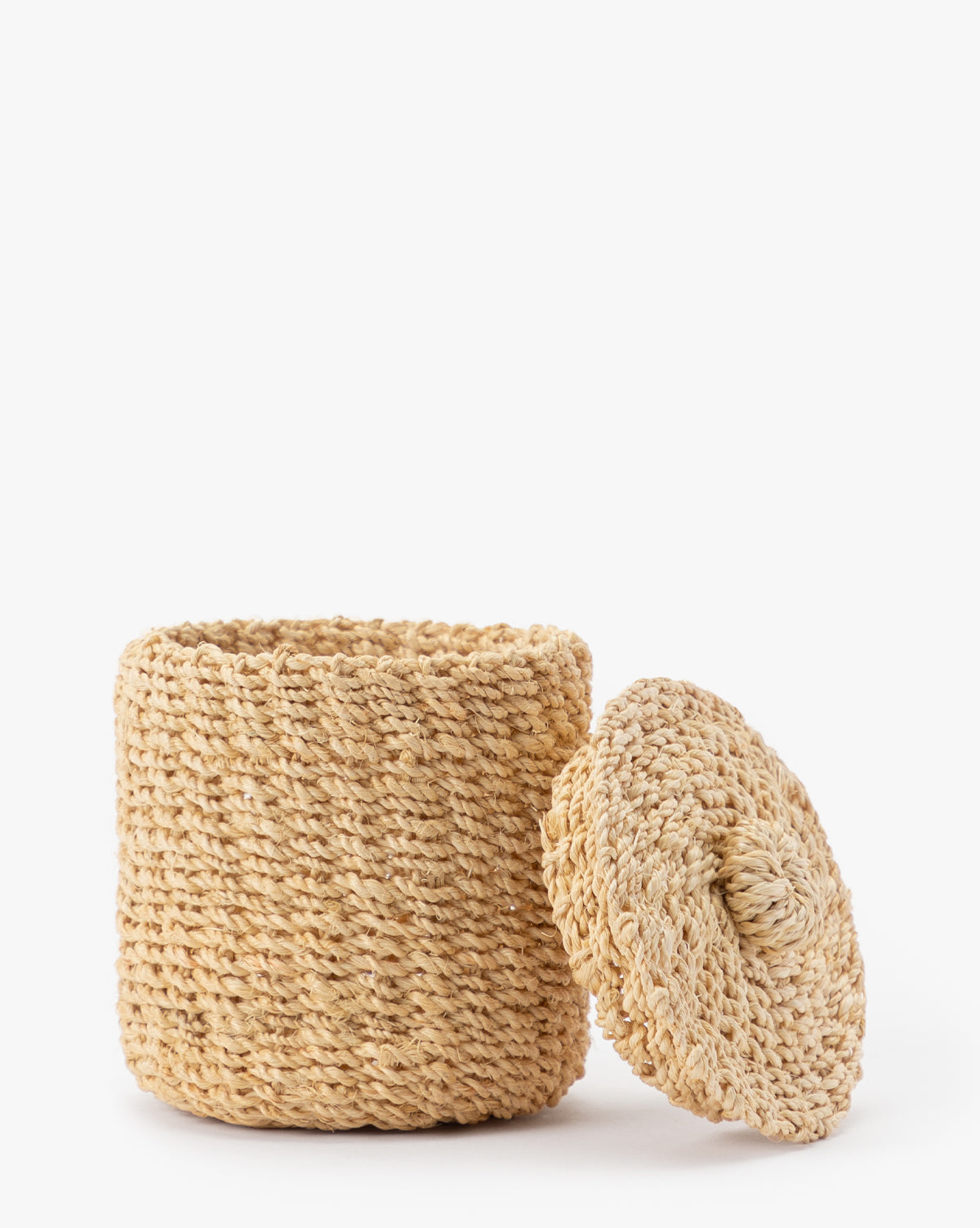 The Thalia Woven Canister, featuring a round shape and matching lid, sits on a white background. Its textured abaca design and open top make it ideal for organic storage or as stylish bathroom counter decor.