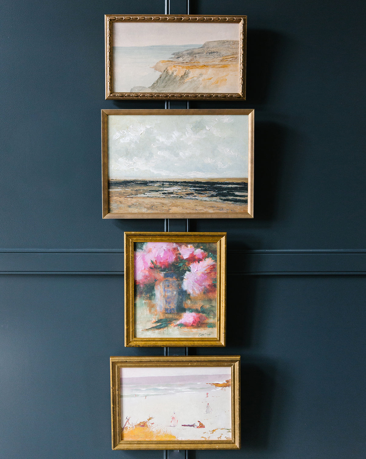 The Dorset set features four vintage-style framed artworks, vertically hung on a dark blue wall, depicting a Dorset cliff scene, the sea, pink flowers, and a beach.