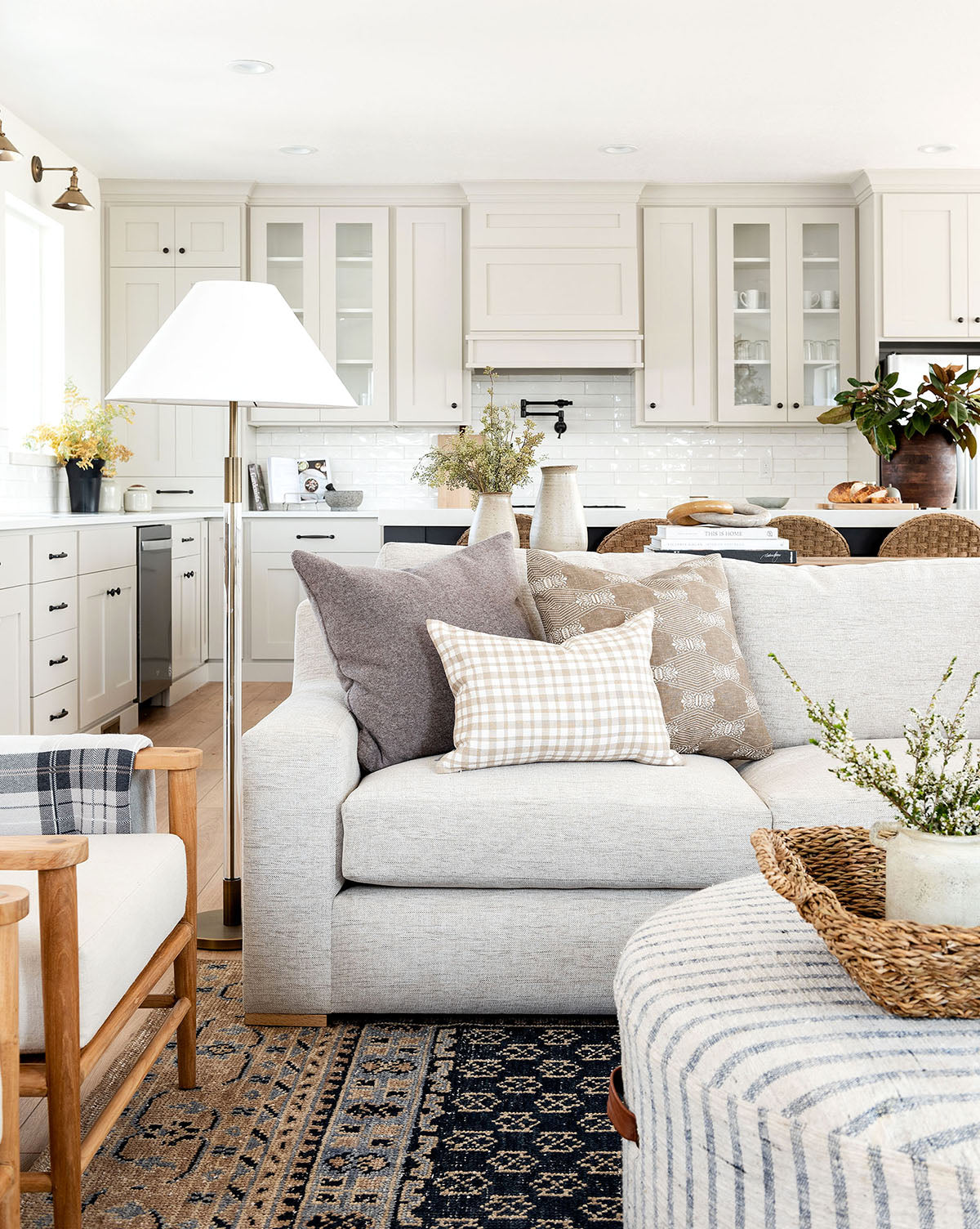 A bright, airy living room and kitchen with light cabinets, a neutral sofa, wooden accents, decorative plants, and the Anya Indigo Hand-Knotted Wool Rug creates a cozy, modern farmhouse vibe, by McGee & Co.