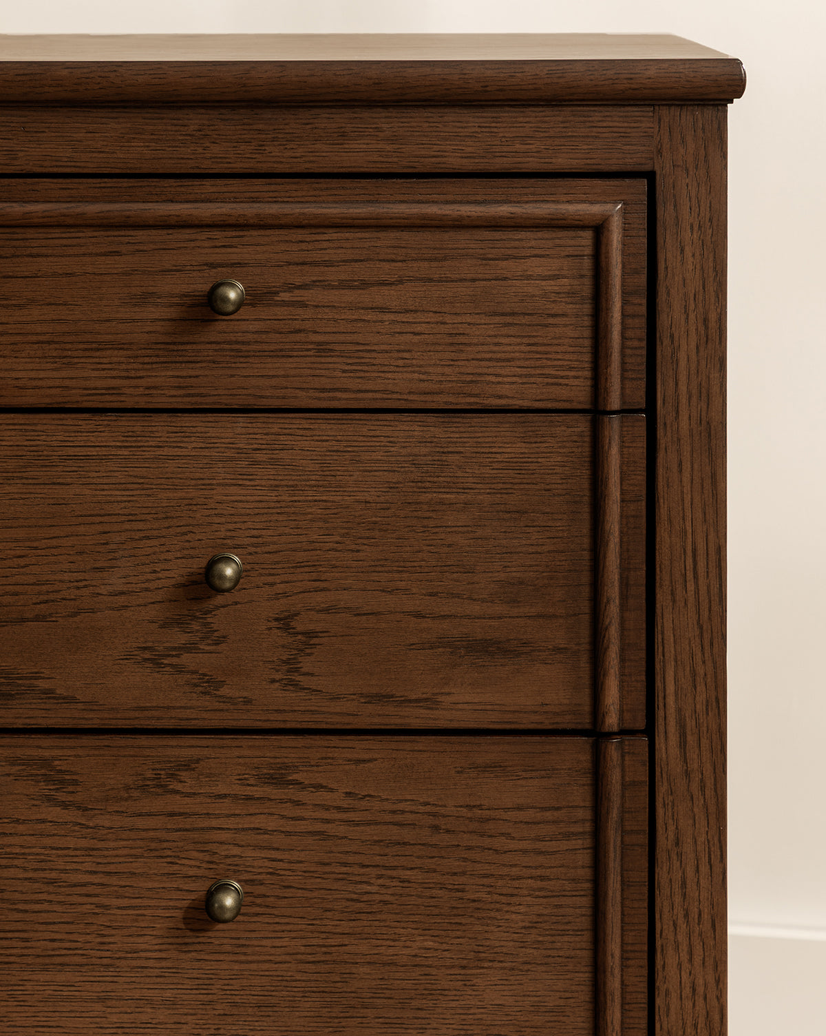 Close-up of the upper half of the Yorkshire Dresser with three drawers, featuring an English oak finish and round metal knobs, by McGee & Co. Visible wood grain enhances its elegant storage design against a light-colored wall.