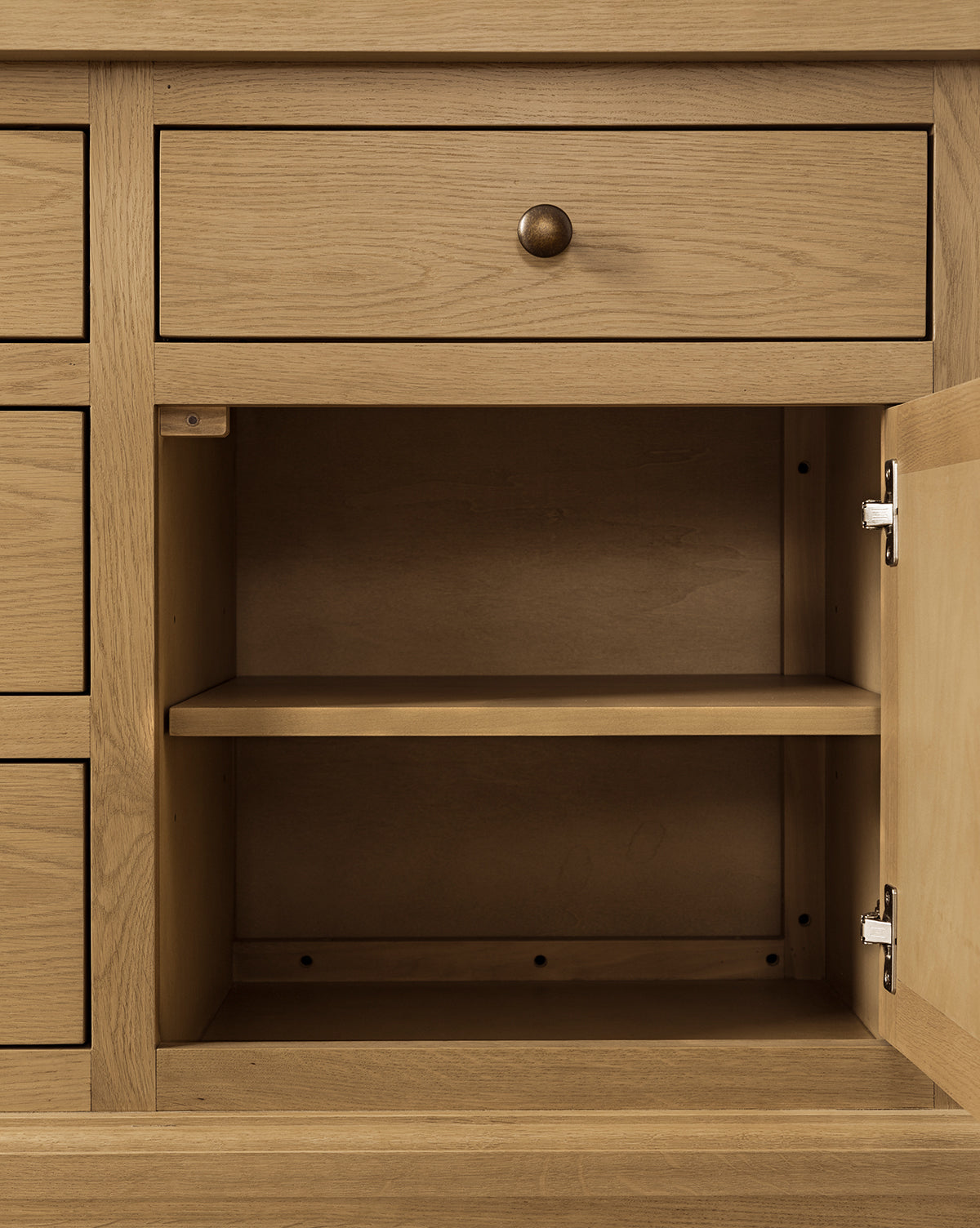 The Adler Oak Cabinet features a light oak finish with an open door revealing spacious interior shelving, while a closed drawer above with a round metal knob enhances its practical design, by McGee & Co.