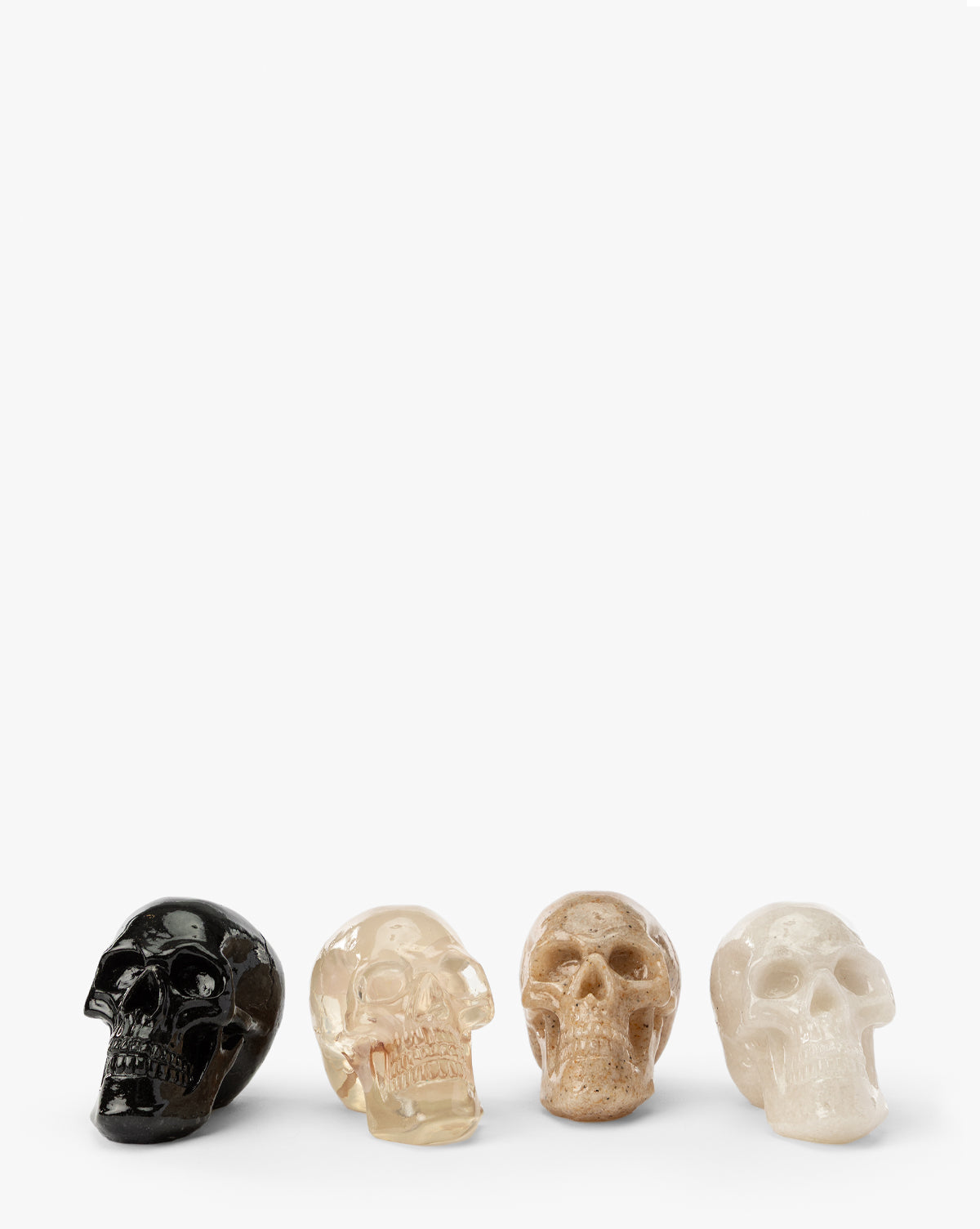 The Assorted Resin Skulls (Boxed Set of 4) features small black, clear, tan, and white skulls arranged in a row—ideal as Halloween decor or as distinctive resin pieces for your collection, displayed on a plain white background by McGee & Co.