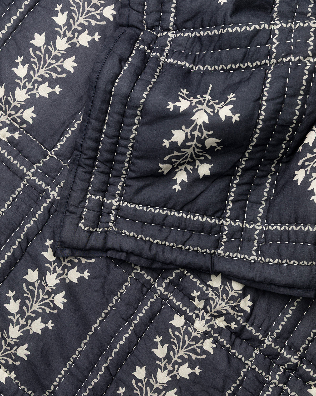 The Atherton Quilt features dark blue fabric adorned with a white floral pattern and decorative white grid stitching, highlighting its handmade artistry in stunning close-up detail, by McGee & Co.