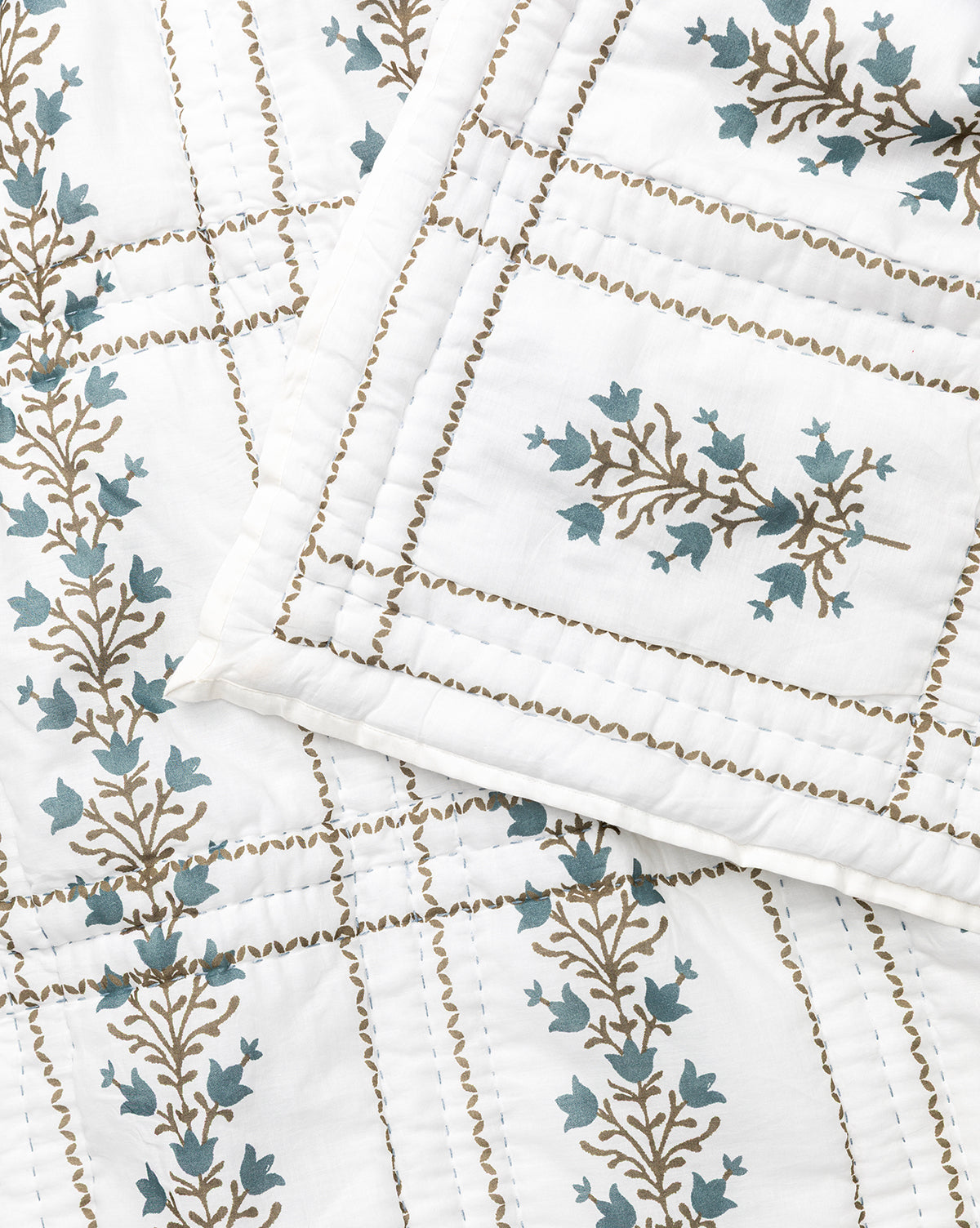 The Atherton Quilt features a stitched grid pattern with brown branches and teal leaves. A matching pillow rests diagonally on the quilt, showcasing the handmade artistry and exquisite floral design, by McGee & Co.