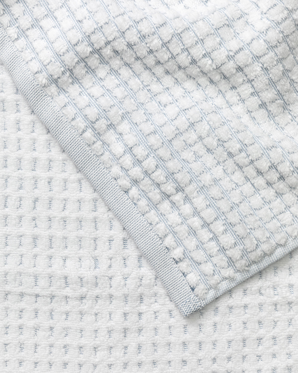 Close-up of a light gray waffle weave towel with a textured pattern and neat edge, displayed on a matching surface—part of our Atrani Gray Organic Bath Collection, by McGee & Co.