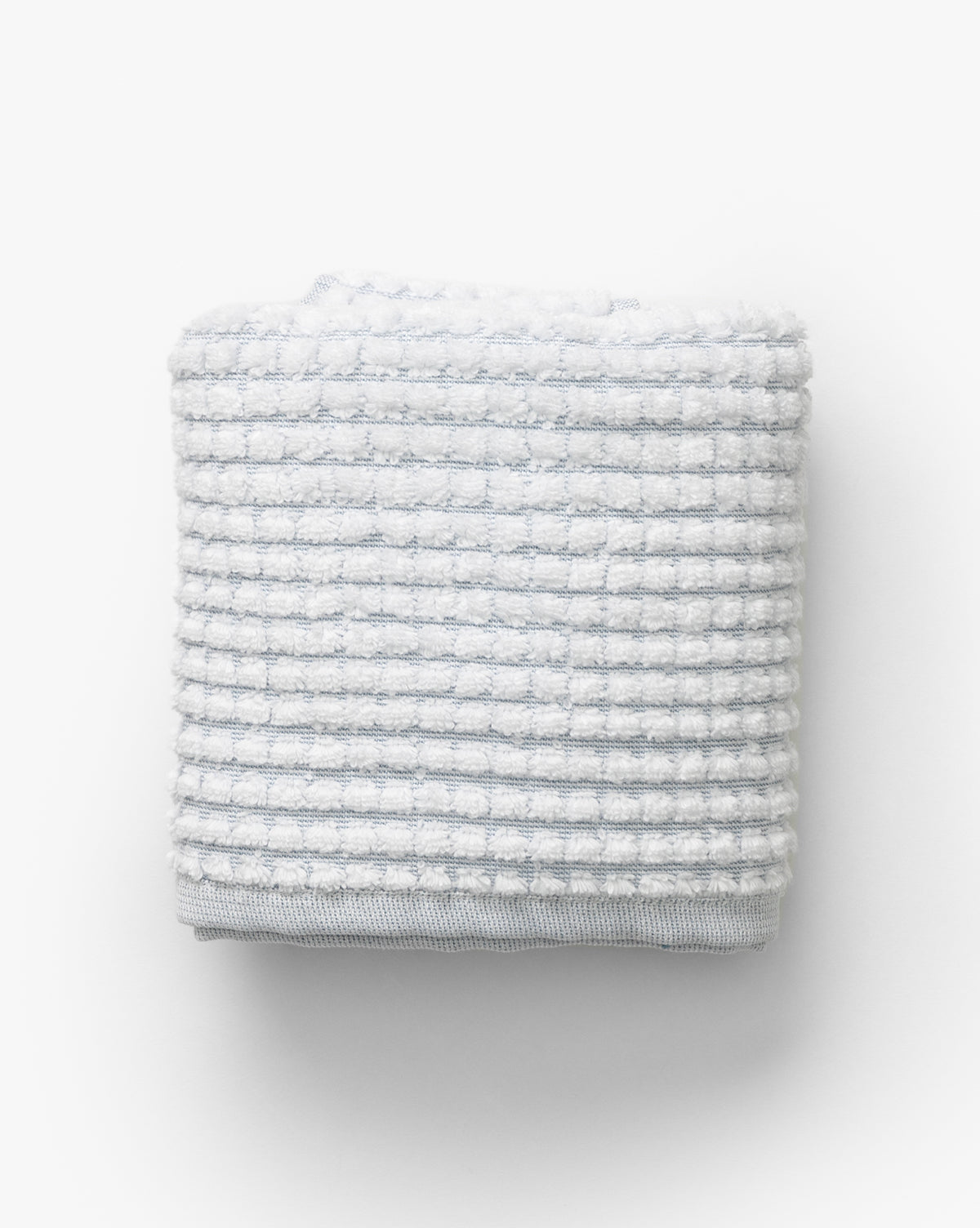 A neatly folded light gray waffle weave towel with a grid pattern from our Atrani Gray Organic Bath Collection, shown against a plain white background by McGee & Co.