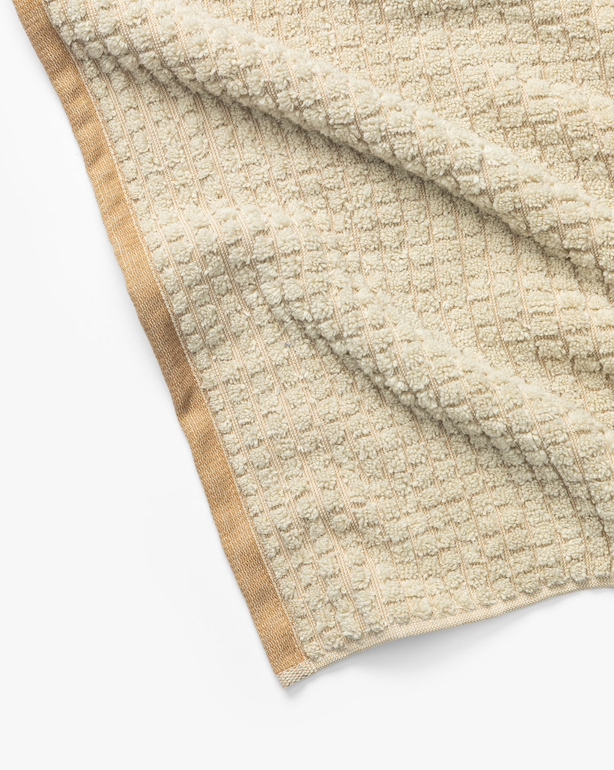 A close-up of a beige textured waffle weave towel from the Atrani Organic Bath Collection, crafted from organic cotton with a solid tan border, laid out on a white surface, by McGee & Co.