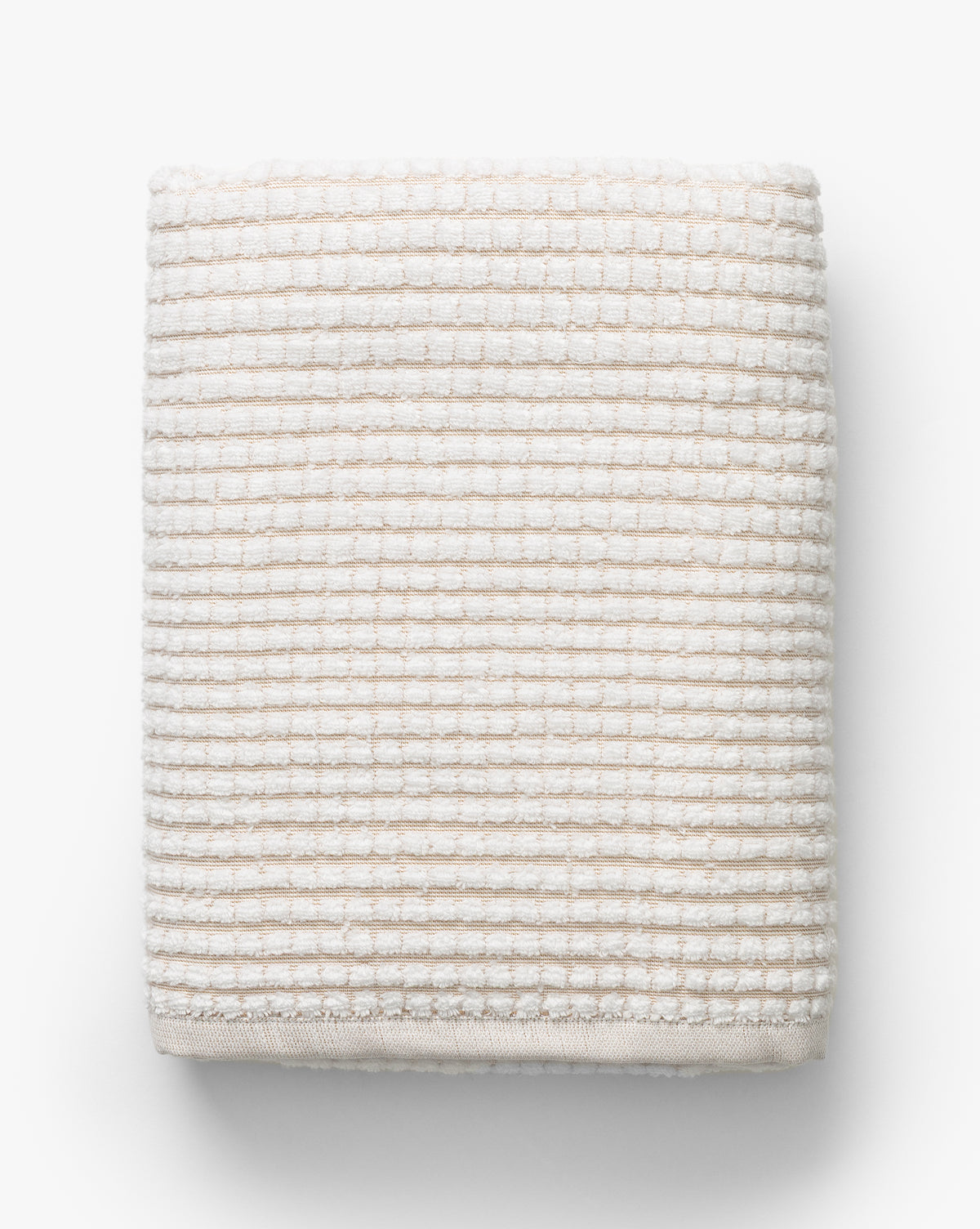 The Atrani Tan Organic Bath Collection features a neatly folded, cream-colored waffle weave towel made from organic cotton with a textured, ribbed pattern, displayed on a white background, by McGee & Co.