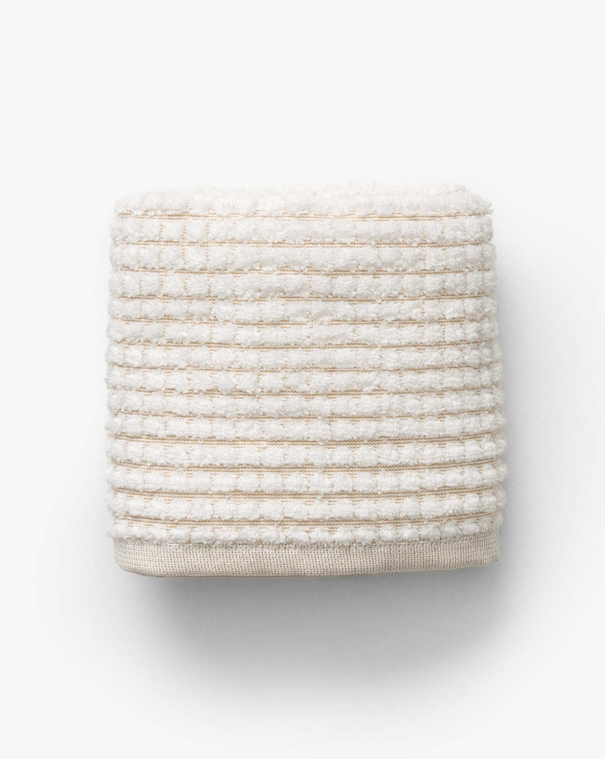 A neatly folded towel from the Atrani Tan Organic Bath Collection, featuring an off-white waffle weave with textured stripes, made from organic cotton and set against a plain white background, by McGee & Co.