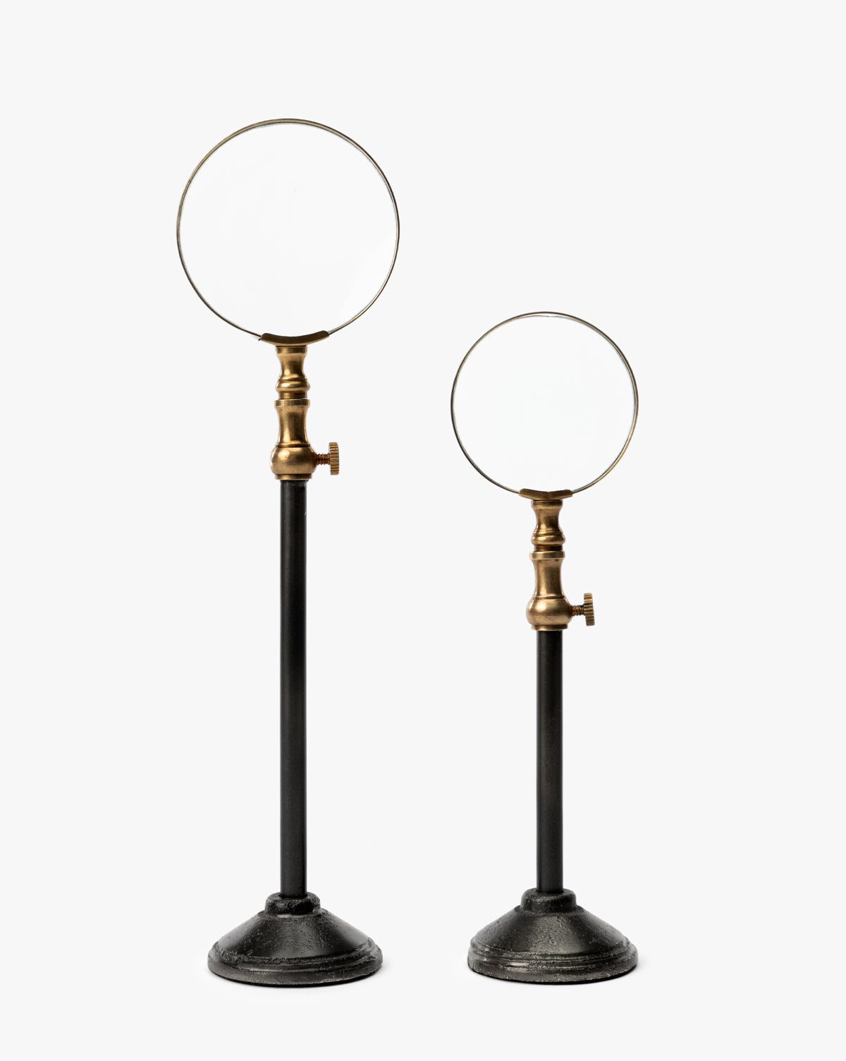 The Barnabas Standing Object features two vintage-style magnifying glasses with burnished brass fittings on tall black metal stands with round bases—a timeless accent for your home decor, shown against a plain white background, by McGee & Co.
