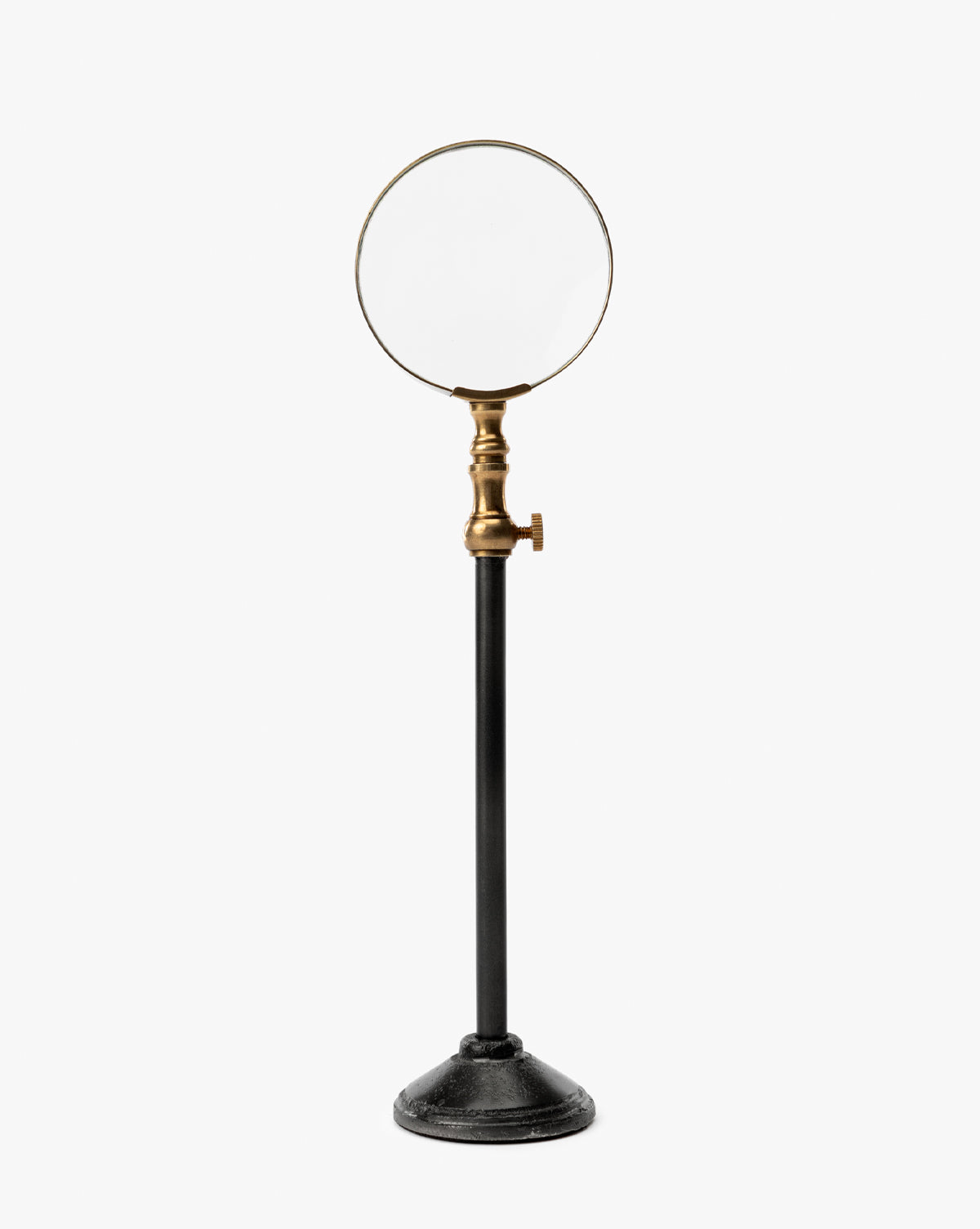 The Barnabas Standing Object features a magnifying glass with a burnished brass holder on a sleek black metal stand, making it an eye-catching piece of home decor against a plain white background, by McGee & Co.