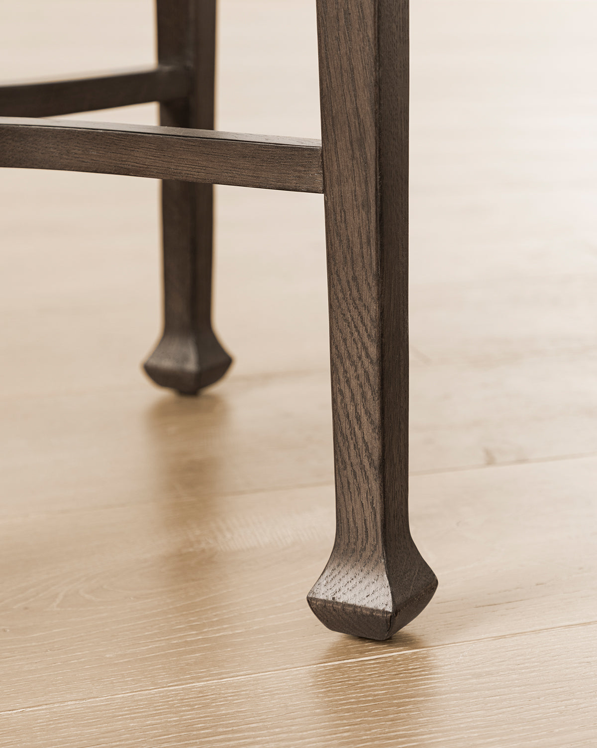 Close-up of the Bradshaw Side Table legs on a light wood floor, showcasing antique-inspired flared feet and a textured satin walnut oak grain, by McGee & Co.