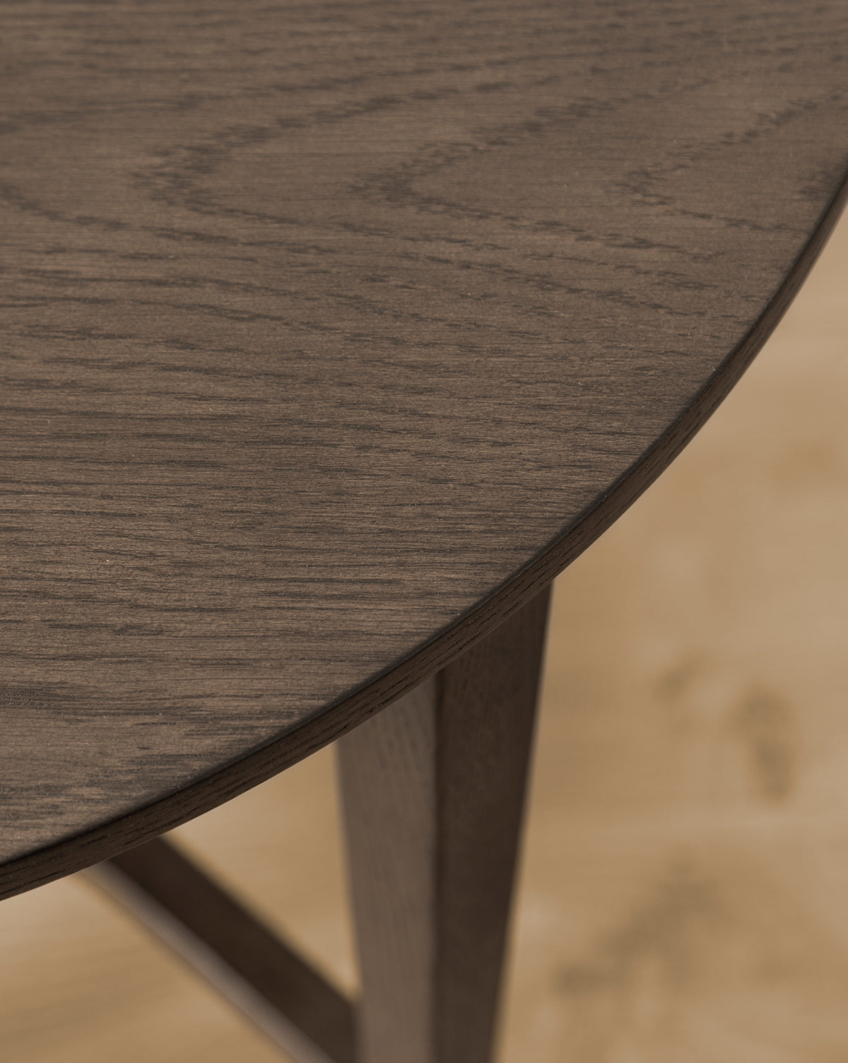 Close-up of the Bradshaw Side Table’s edge, highlighting its smooth satin walnut oak finish and one angled leg resting on a light-colored floor by McGee & Co.