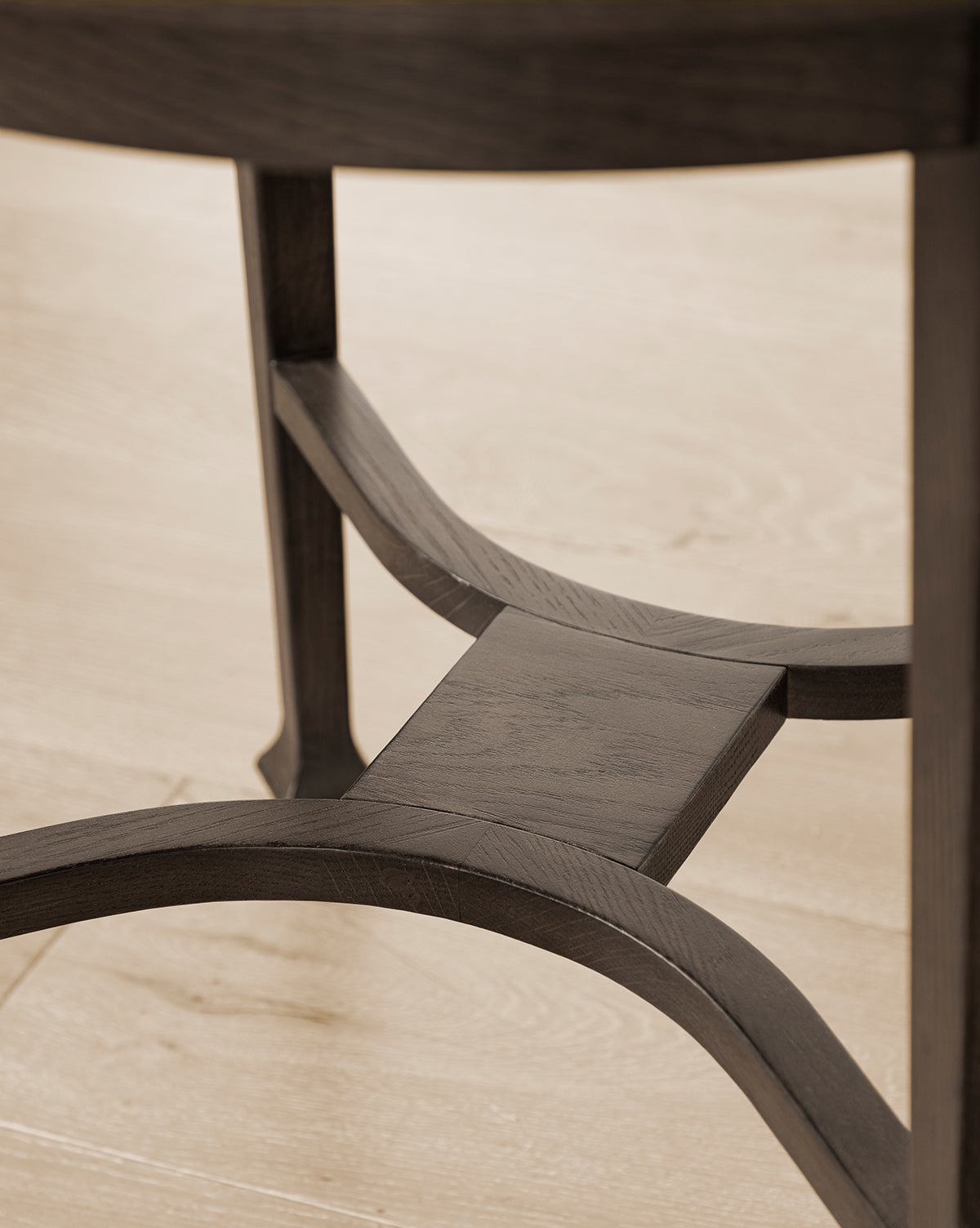 Close-up of a wooden chair’s lower section, showcasing its curved, antique-style legs and satin walnut oak support braces. The chair is placed on a light wood floor next to the Bradshaw Side Table, by McGee & Co.