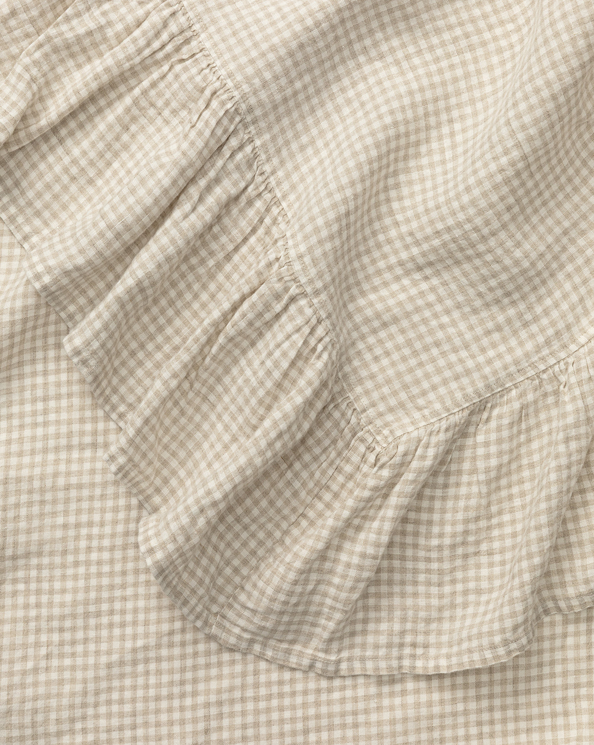 A close-up of the Catania Linen Ruffle Tablecloth in beige and white gingham, showcasing its soft, textured small checks and ruffled edge, by McGee & Co.
