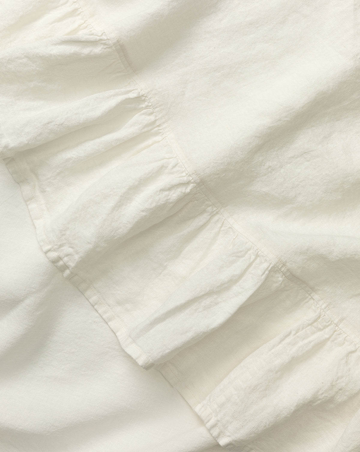 Close-up of the Catania Linen Ruffle Tablecloth in white, featuring a diagonal ruffled seam that highlights its soft texture and gentle folds, by McGee & Co.