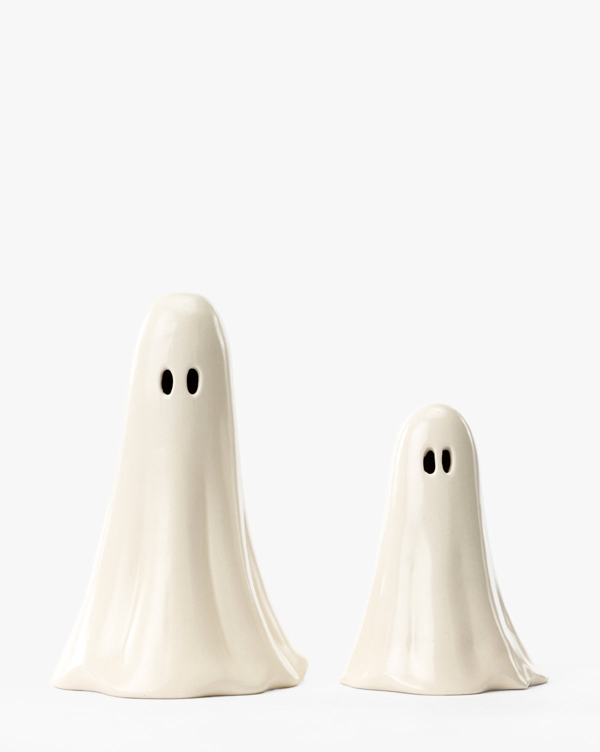Two Ceramic Ghost Figures—one tall, one short—with smooth white surfaces and black oval eyes stand together, perfect as charming Halloween decor or spooky home accents, by McGee & Co.