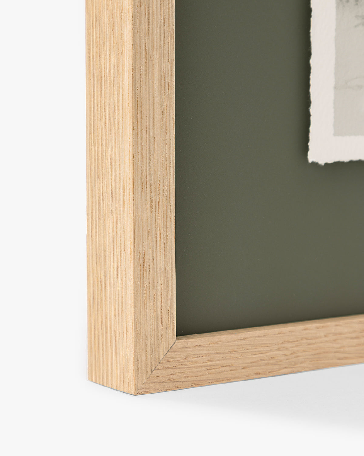 Close-up of the light oak frame of Cove in Charcoal, showing visible wood grain and a rough-edged paper—ideal home decor to highlight your favorite charcoal sketch against a dark green background, by McGee & Co.