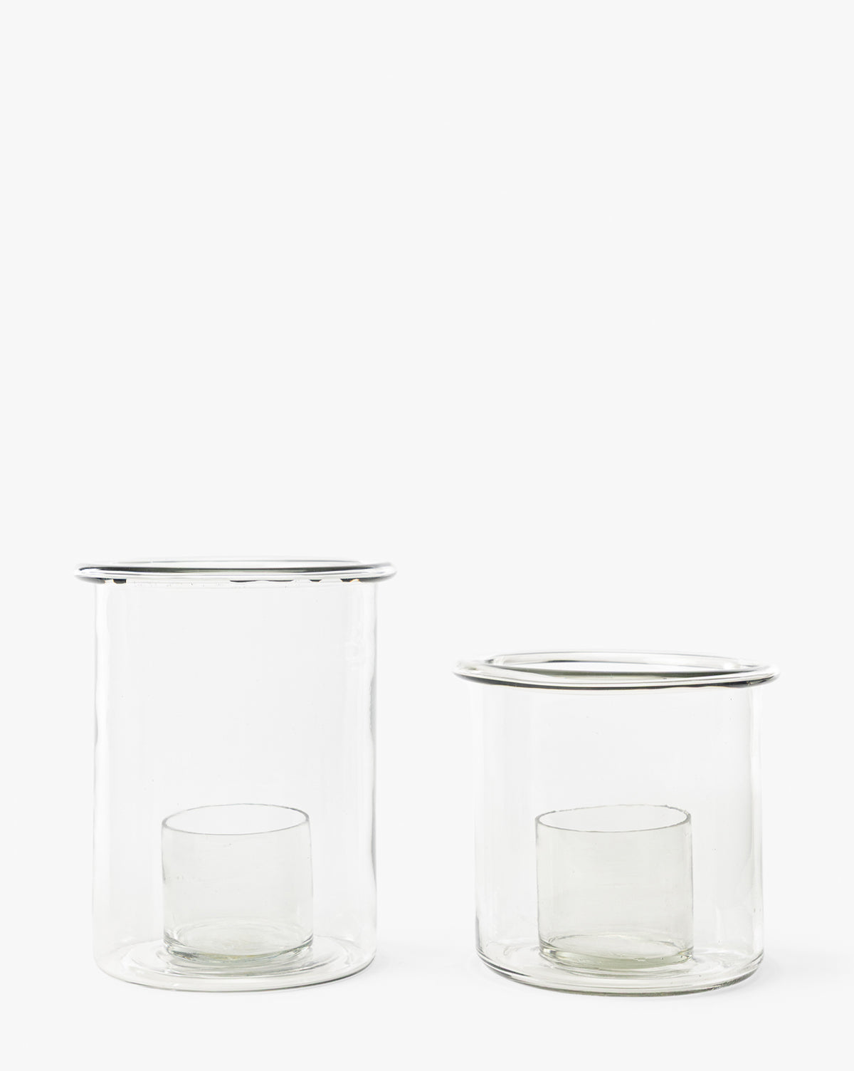The Cyrus Hurricane set features two clear glass candle holders of varying heights, each with an inner cylindrical glass, shown side by side on a white background—ideal for elegant home decor, by McGee & Co.