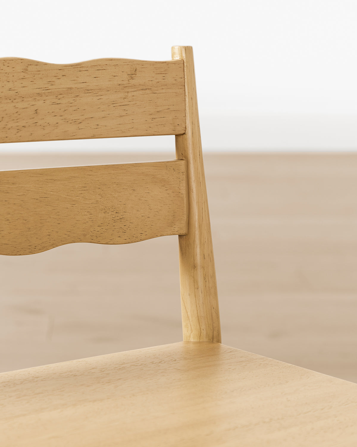Close-up of a Darcy Kids Chair from the Darcy Kids Chairs (Set of 2), featuring a light wood finish, backrest with two horizontal slats—one with a wavy edge—and a softly blurred background that highlights this stylish play chair, by McGee & Co.