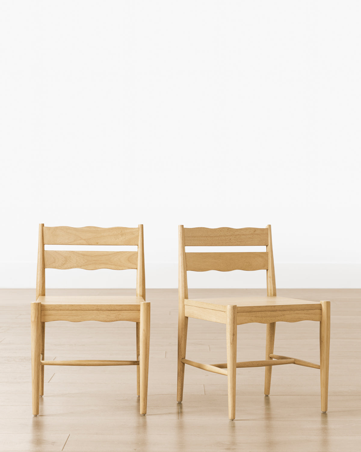 Two Darcy Kids Chairs (Set of 2), made from light-colored wood with wavy slatted backrests, stand on a light wood floor against a plain white wall—stylish and sturdy seating for any kids’ play area, by McGee & Co.
