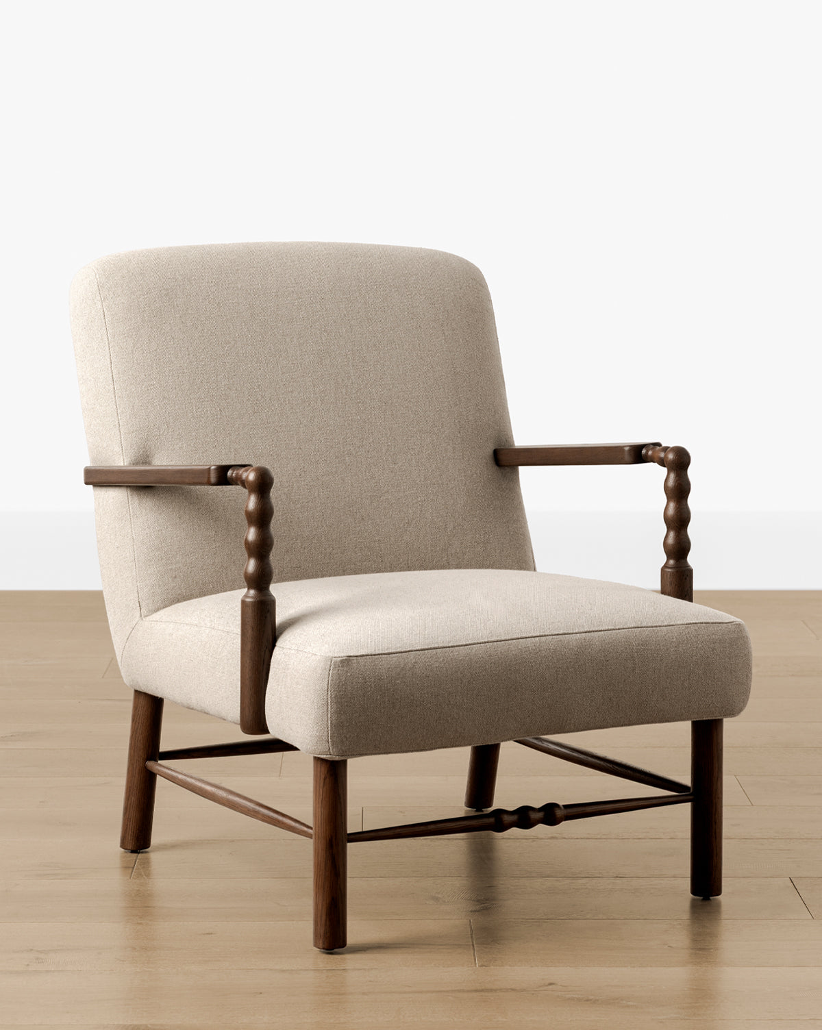 The Earnshaw Lounge Chair has neutral upholstery, wooden legs and armrests in an English oak finish, set on a light wood floor against a plain white wall, by McGee & Co.