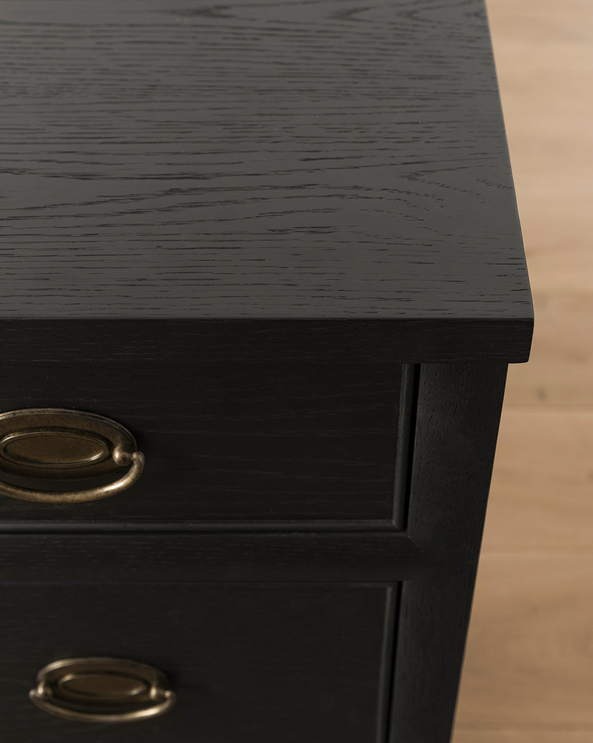 Close-up of the Edward Dresser in Black Ash with brass oval handles, showing visible wood grain on the surface and drawers. Ideal for bedroom storage, it is pictured standing on a light wood floor, by McGee & Co.
