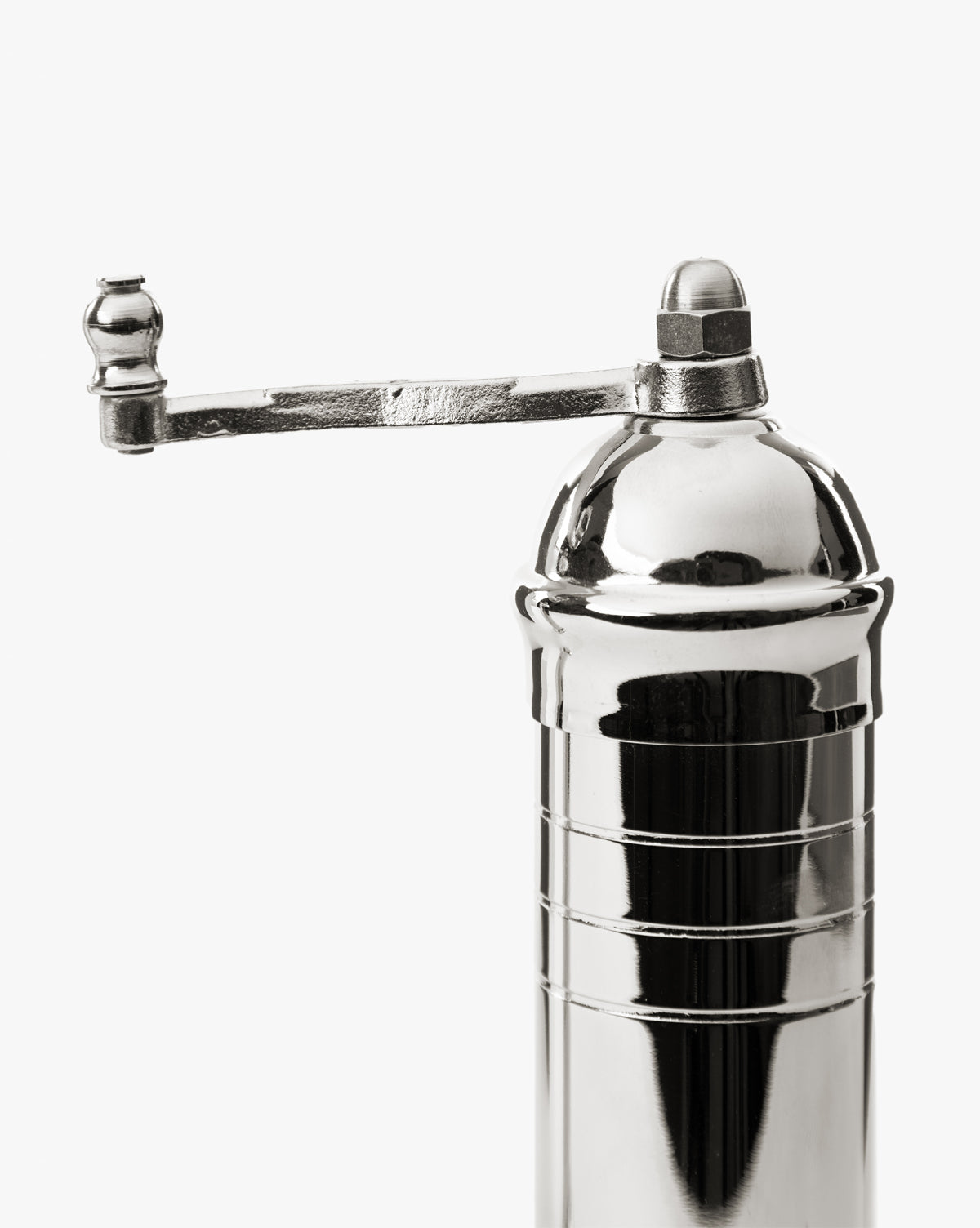 A close-up of the European Chrome Salt Mill features a shiny, metallic body, adjustable steel grinding mechanism, and a horizontal hand-crank handle on top, all set against a plain white background, by McGee & Co.