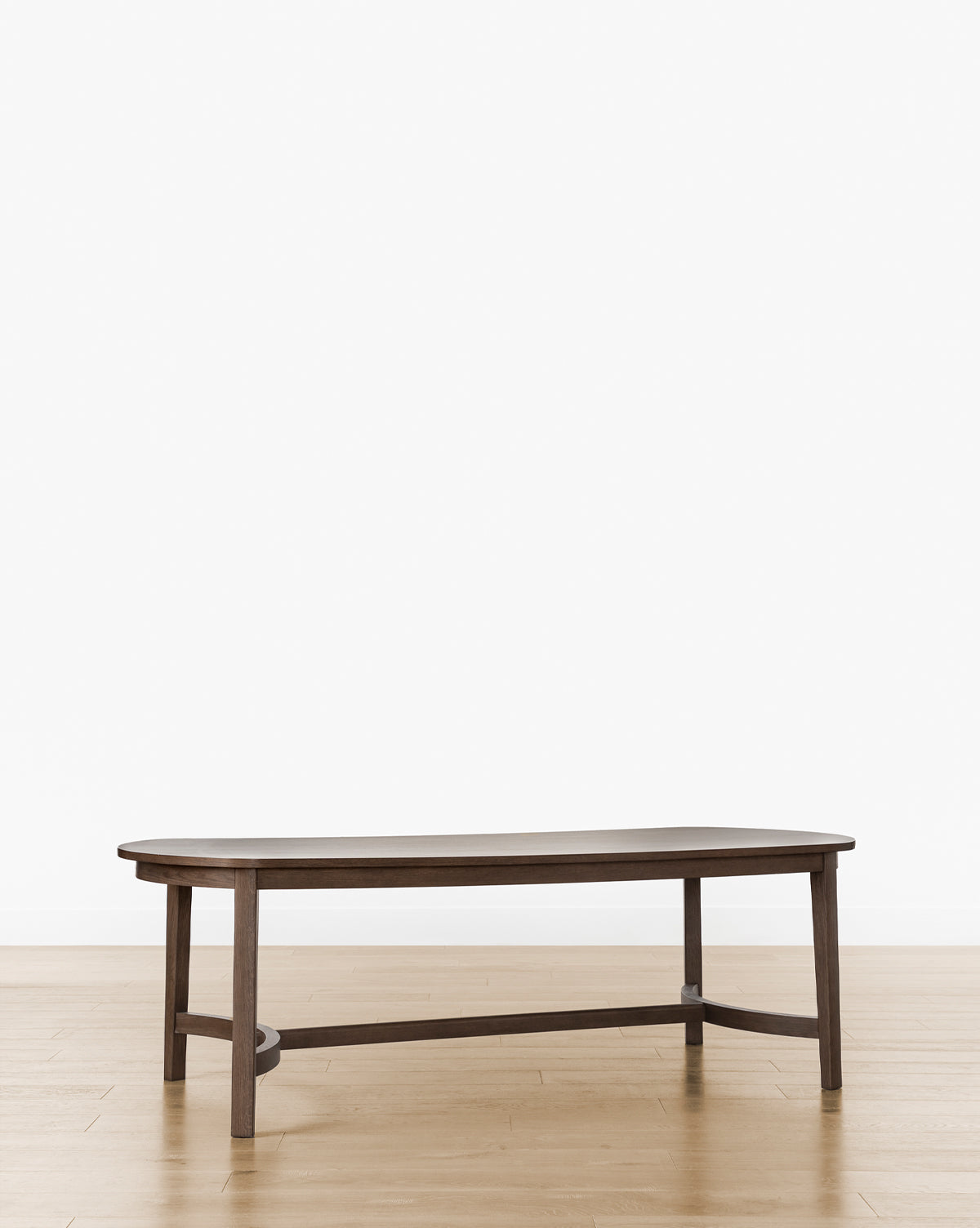 The Gardiner Dining Table features a modern design with a dark Walnut Oak finish, an irregular oval top, and angled legs, by McGee & Co. It is shown on a light wood floor against a plain white background.