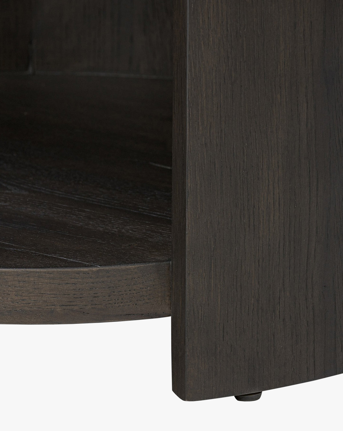 Close-up of the lower corner of the Glenndon Oak Nightstand, featuring a black oak finish with visible wood grain, curved base, vertical panel, and a small black floor protector by McGee & Co.