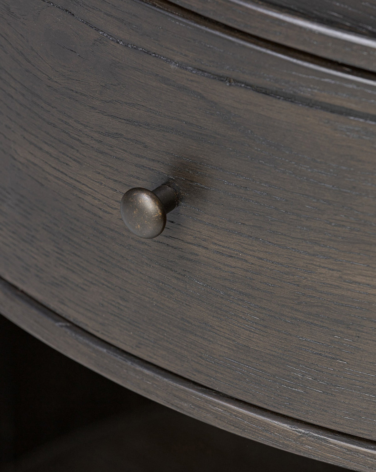 Close-up of the Glenndon Oak Nightstand’s black-finished drawer, featuring a round metal knob. The elegant wood grain and slightly curved front bring modern sophistication to this bedside table by McGee & Co.