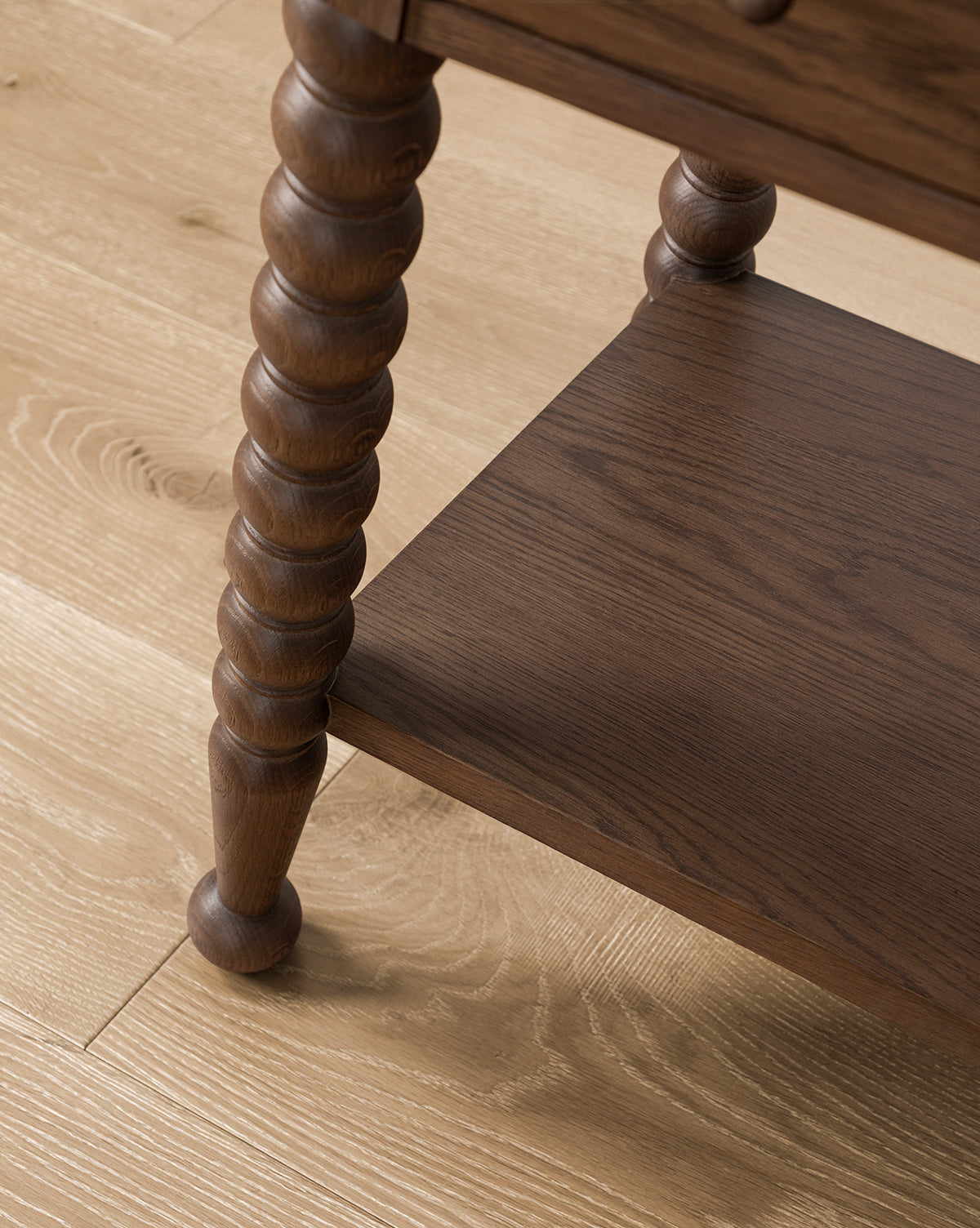 Close-up of the Heathcliff Consoles bobbin-style leg with turned detailing and lower shelf, displayed on a light wood floor, by McGee & Co.